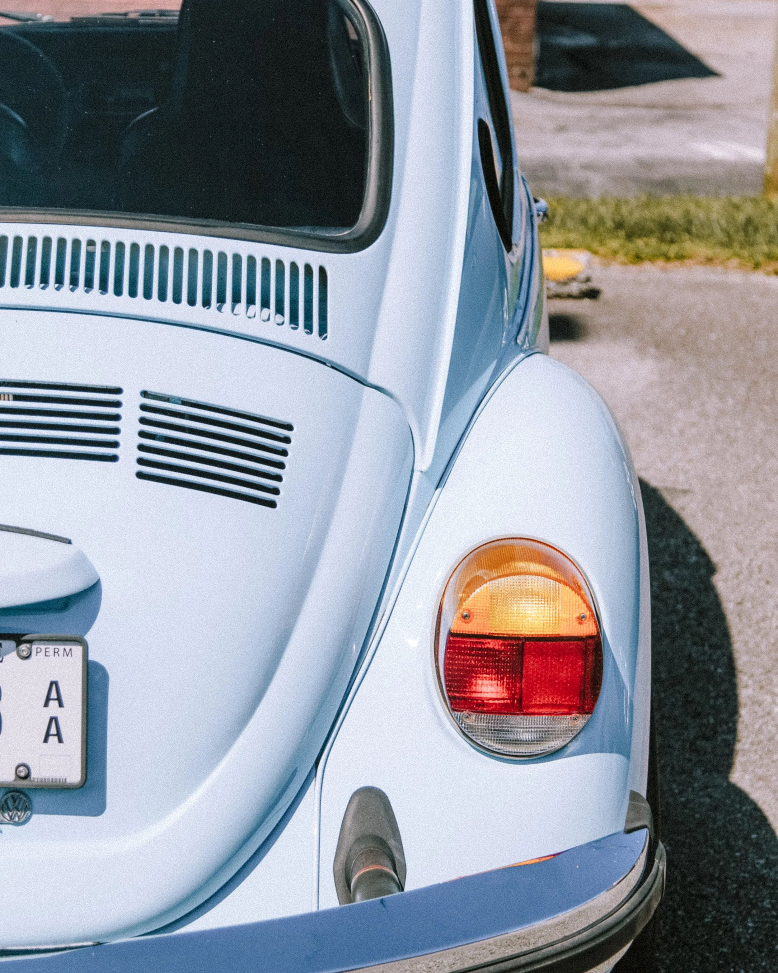 Close-up of the rear of a vintage light blue Volkswagen Beetle, showing the taillight, exhaust pipe, rear wheel, and part of the license plate.