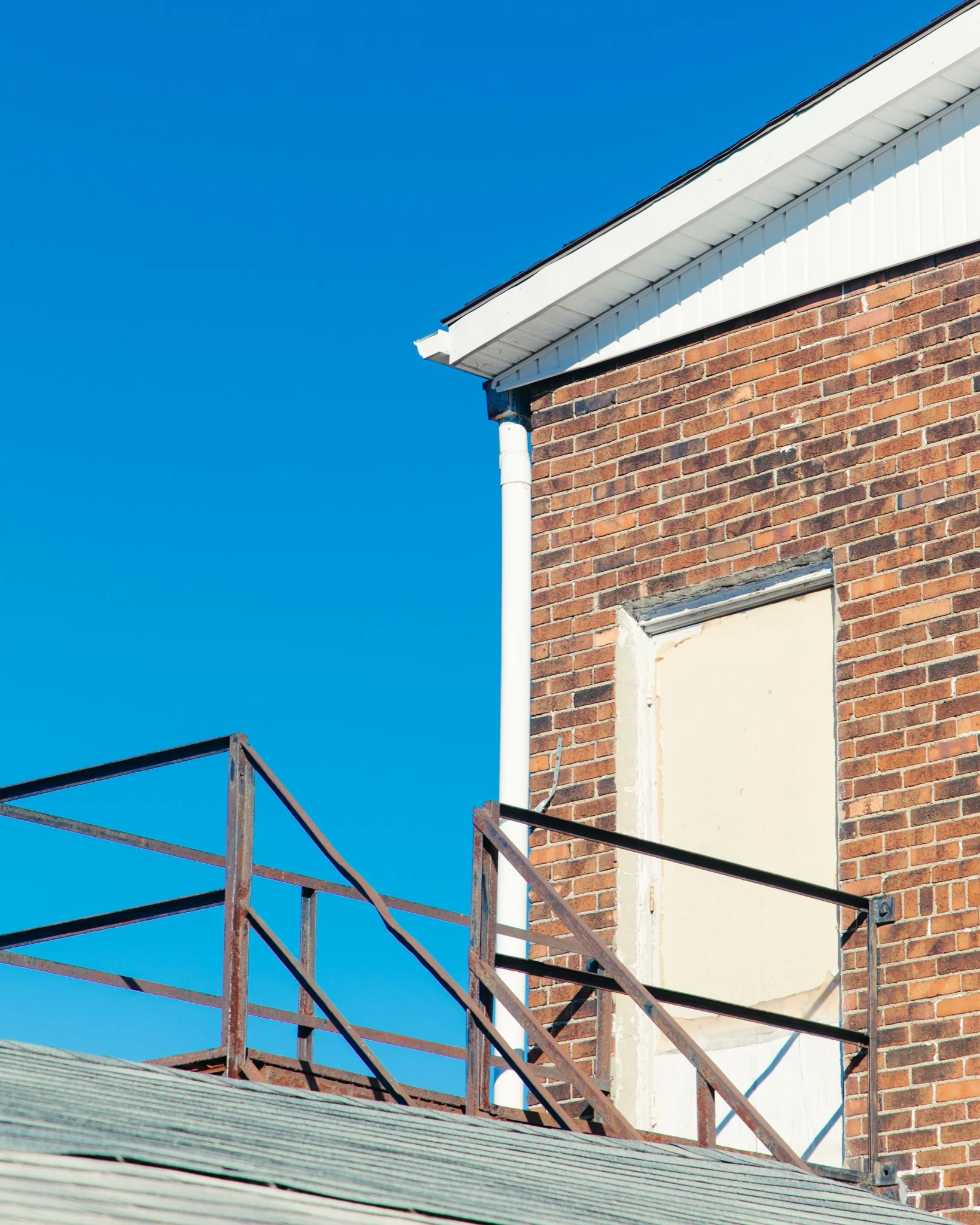 Close-up of a brick building under construction with scaffolding and a white gutter against a clear blue sky.