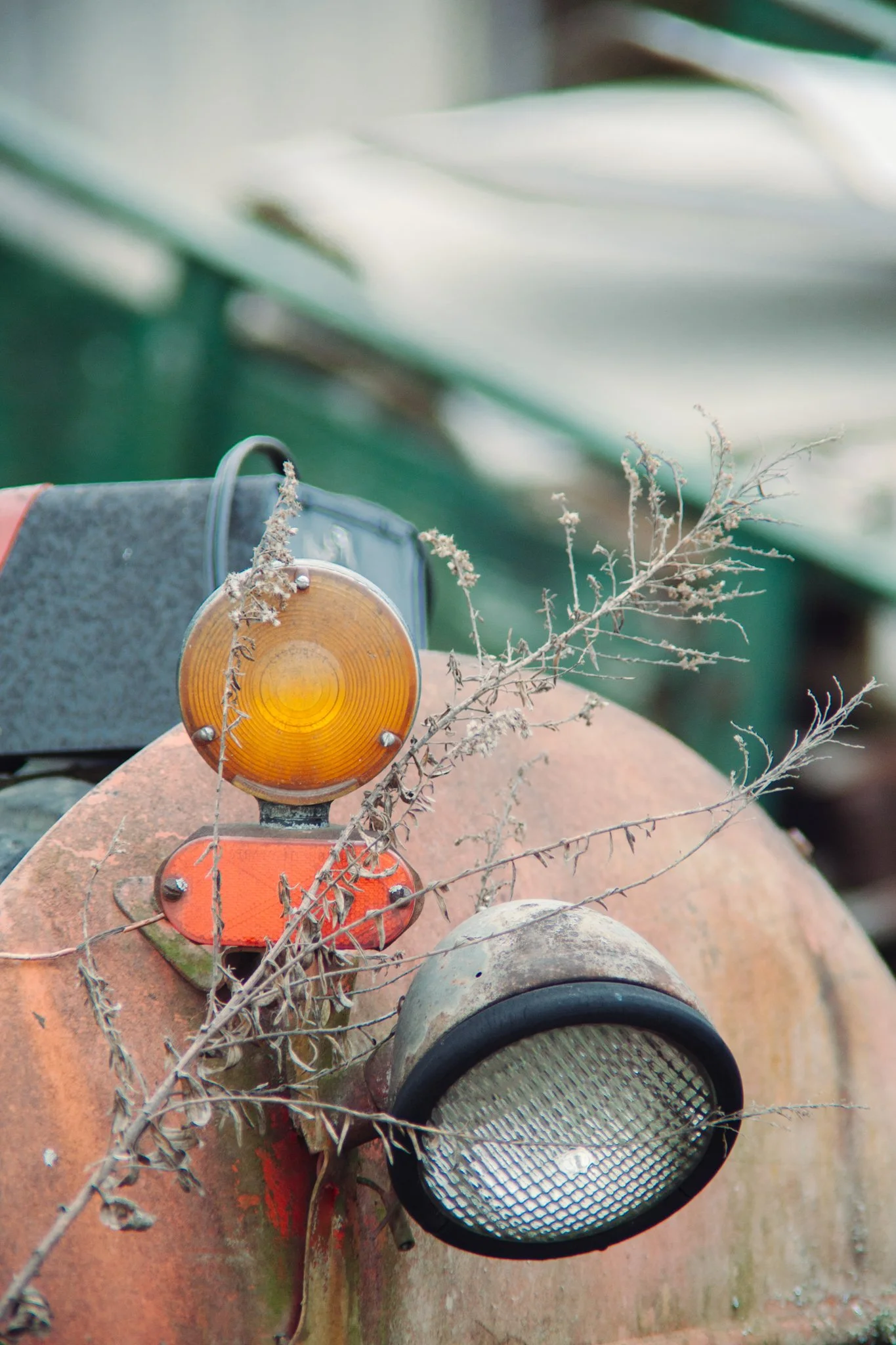 Close-up of an old, rusty tractor with various lights and a dry plant growing on it, set outdoors.