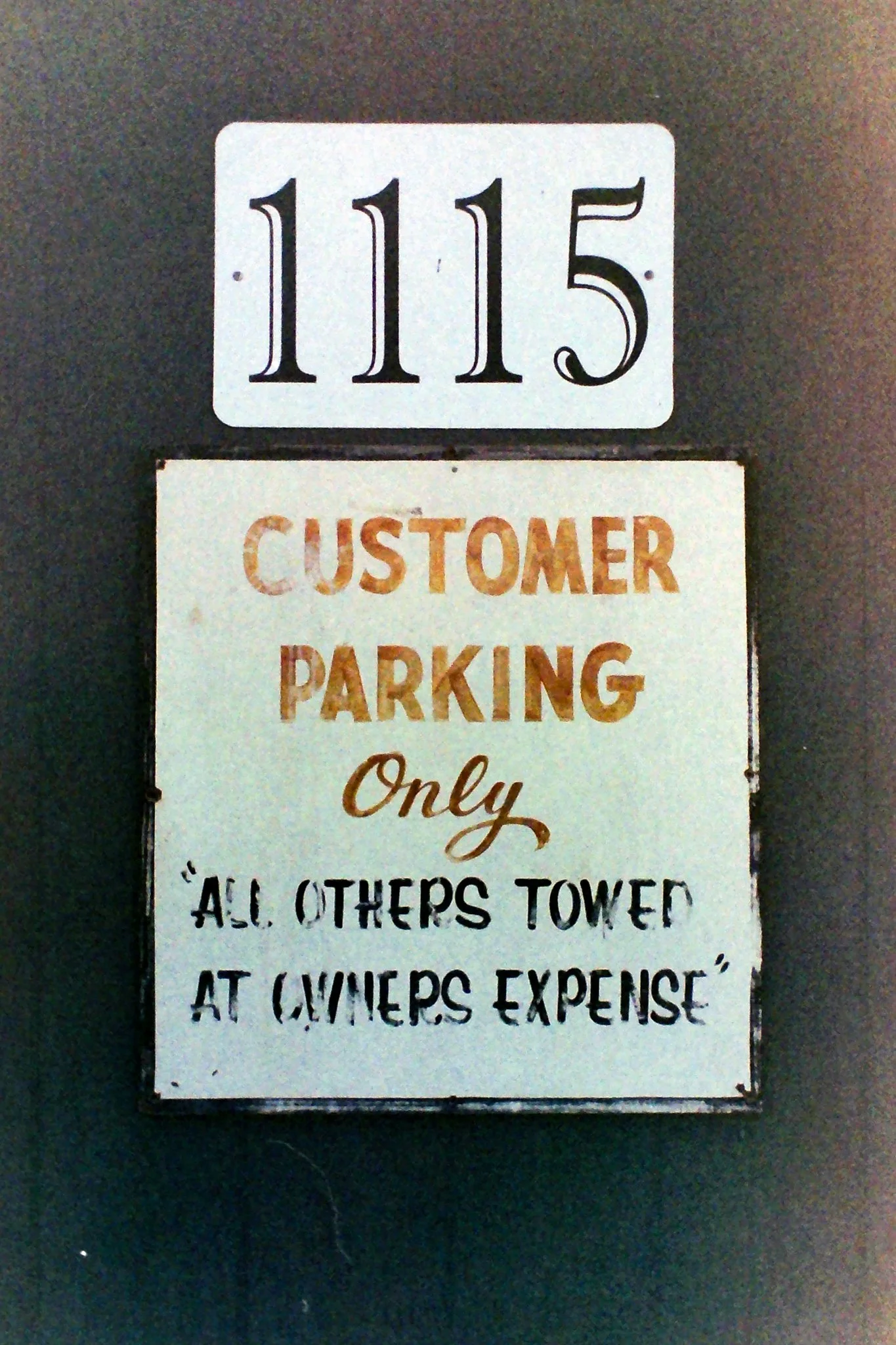 A sign displaying the number 1115 and a notice for customer parking, with a humorous message about others towing at the owner's expense.