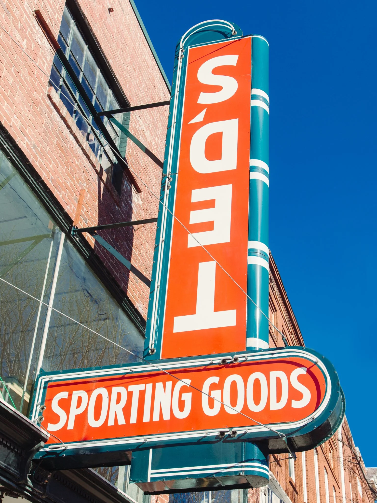 A vertical sign reading 'SPORTING GOODS' hangs outside a brick building against a clear blue sky.