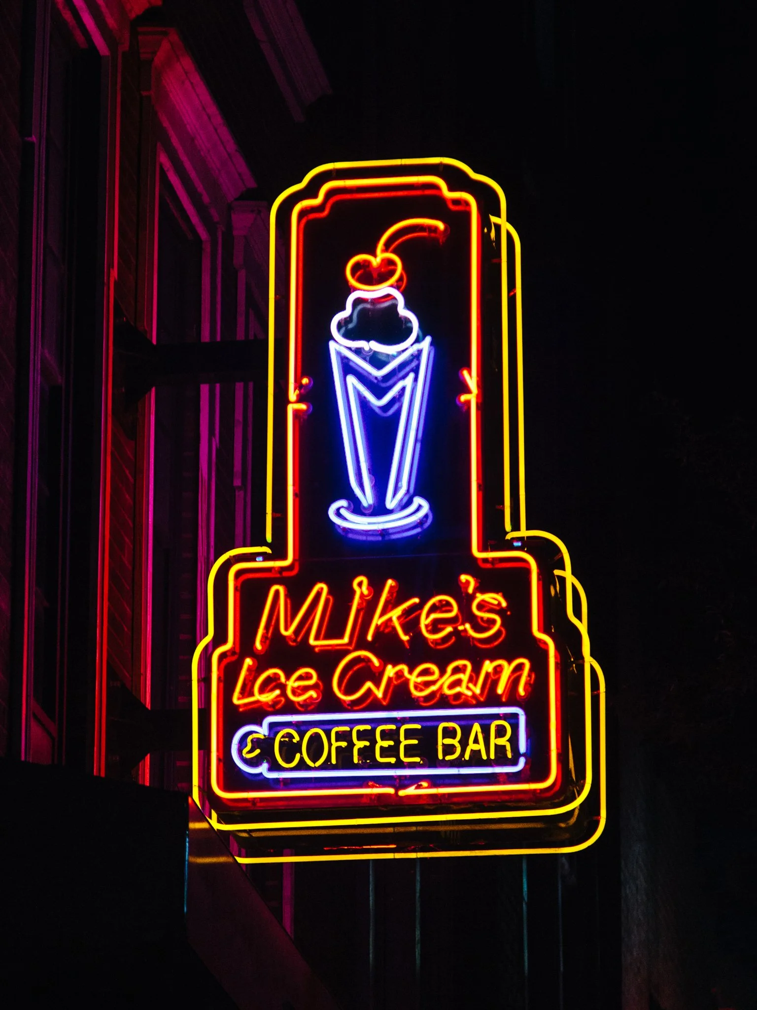 Neon sign advertising a scoop ice cream, with the words "Mike's Ice Cream" and "Coffee Bar," along with a graphic of an ice cream cone with a cherry on top.