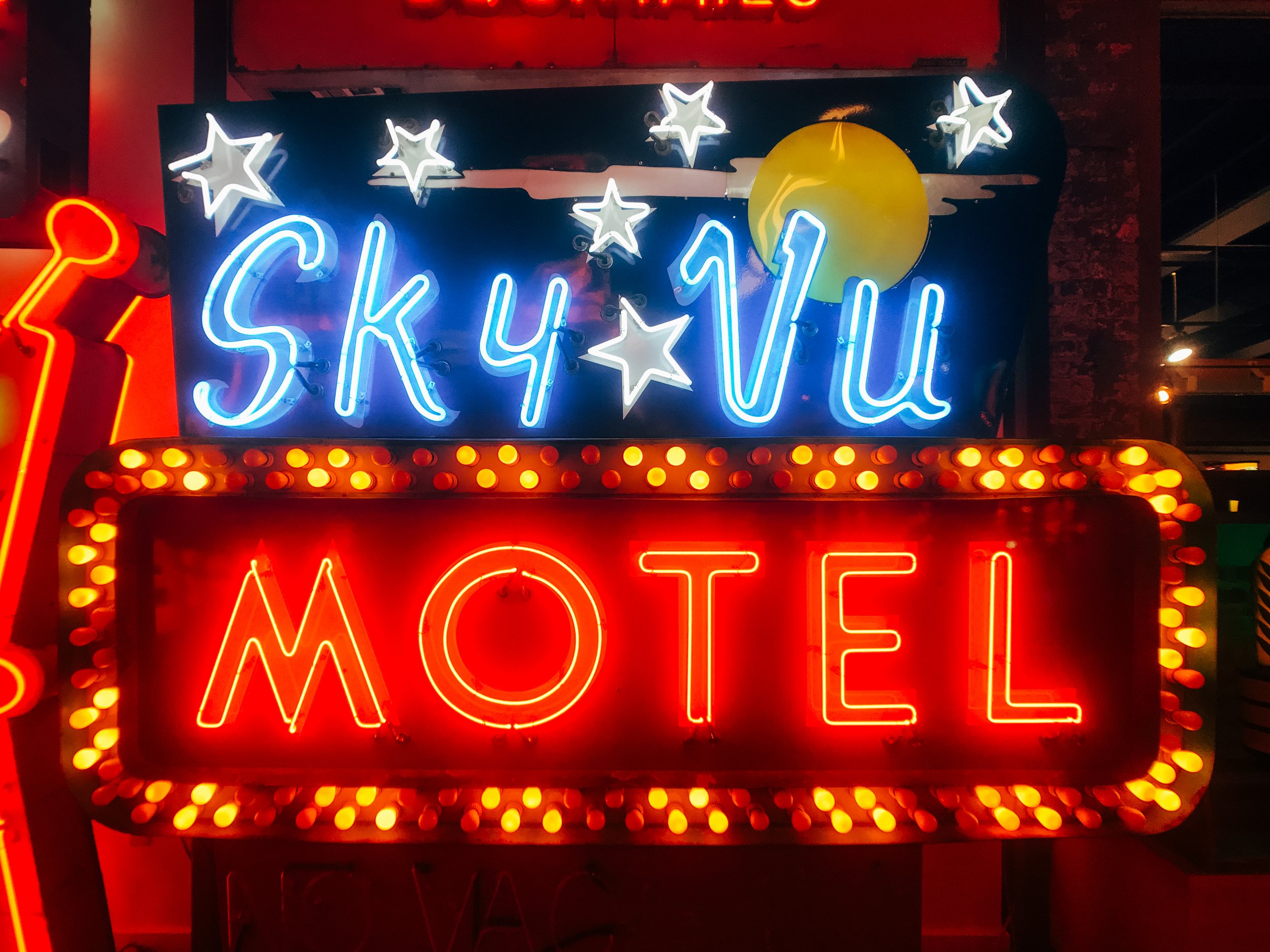 A neon sign with the word 'SKYLUV' in blue, accompanied by white stars and a yellow moon in the background, surrounded by orange bulbs.