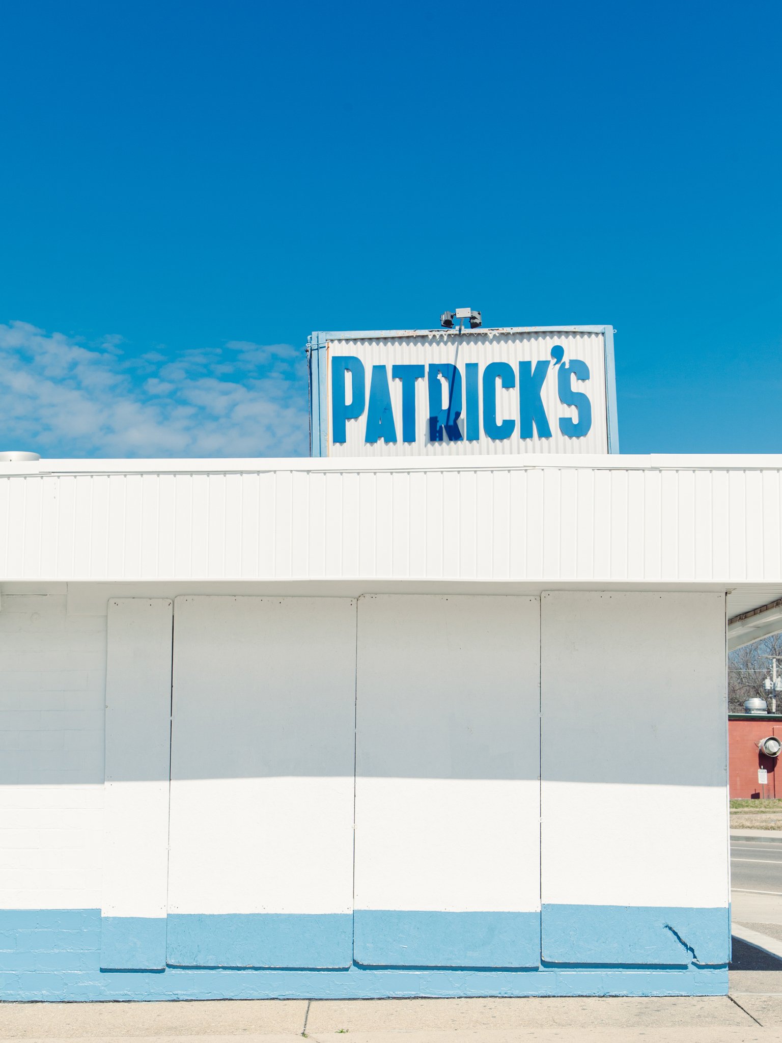 A white building with a blue sign that reads 'Patrick's' against a cloudy blue sky.