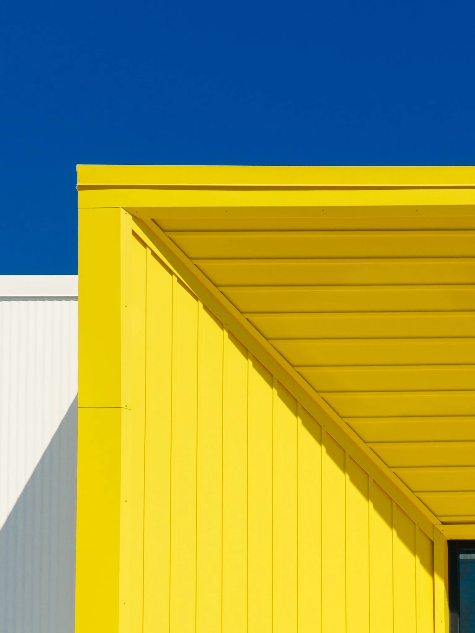 Close-up of a yellow structure with diagonal slats against a bright blue sky.