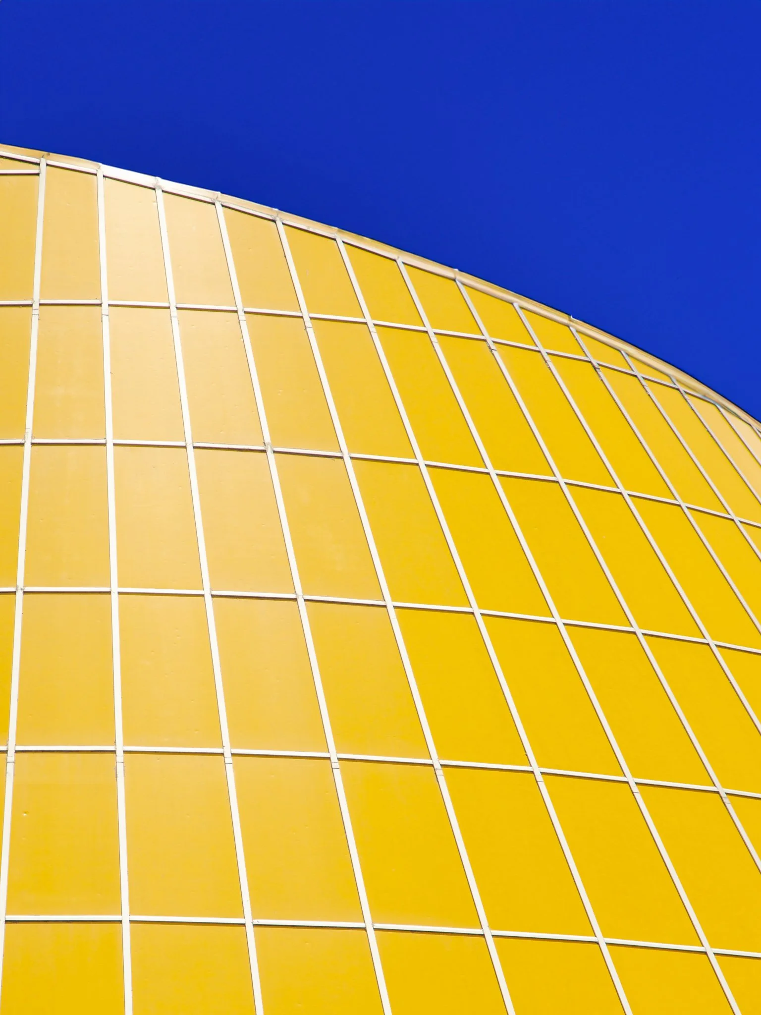 A modern yellow building with a curved domed roof and white structural lines against a deep blue sky.