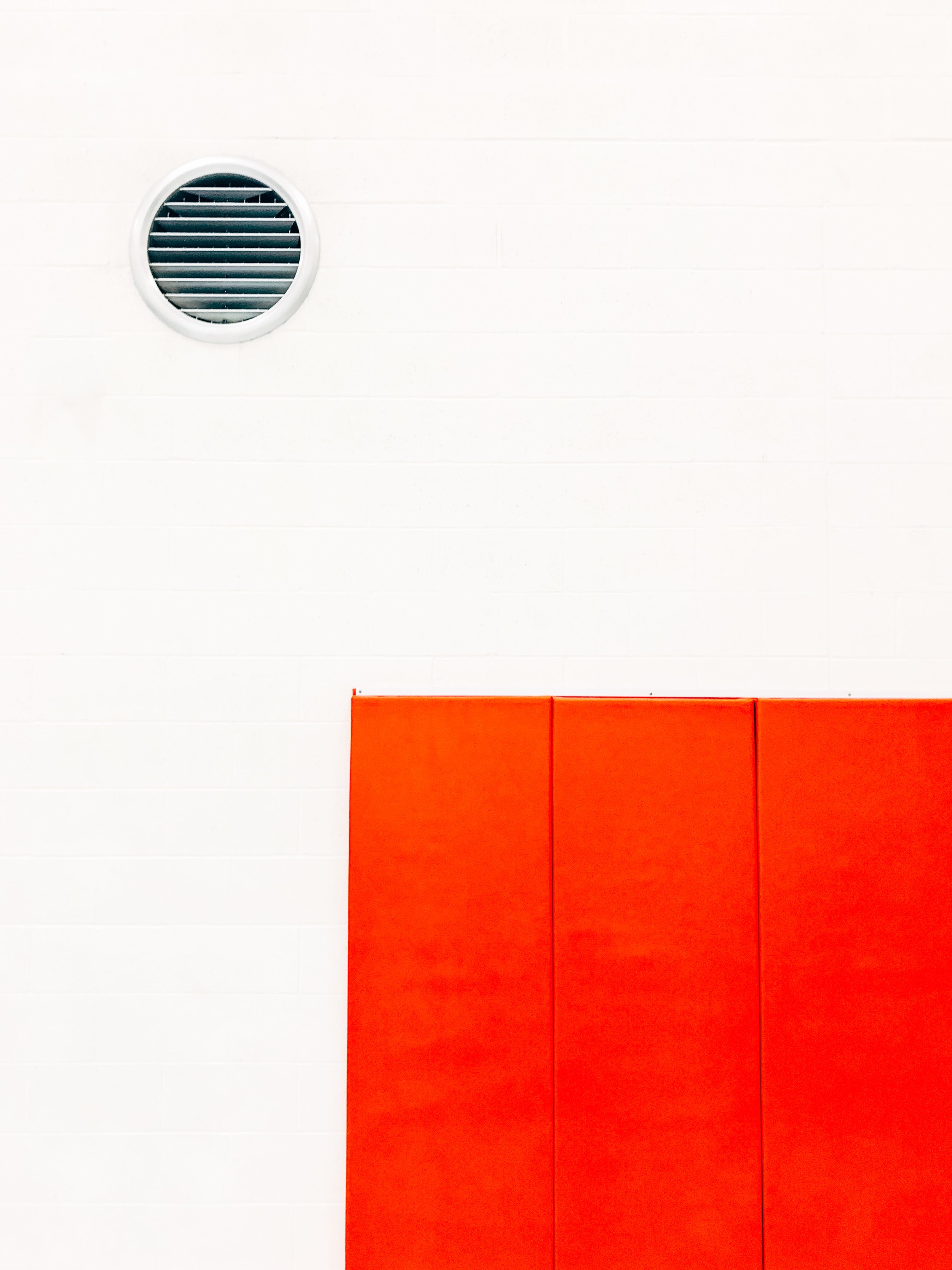 A white wall with a round ventilation vent near the top left and a red padded section at the bottom.