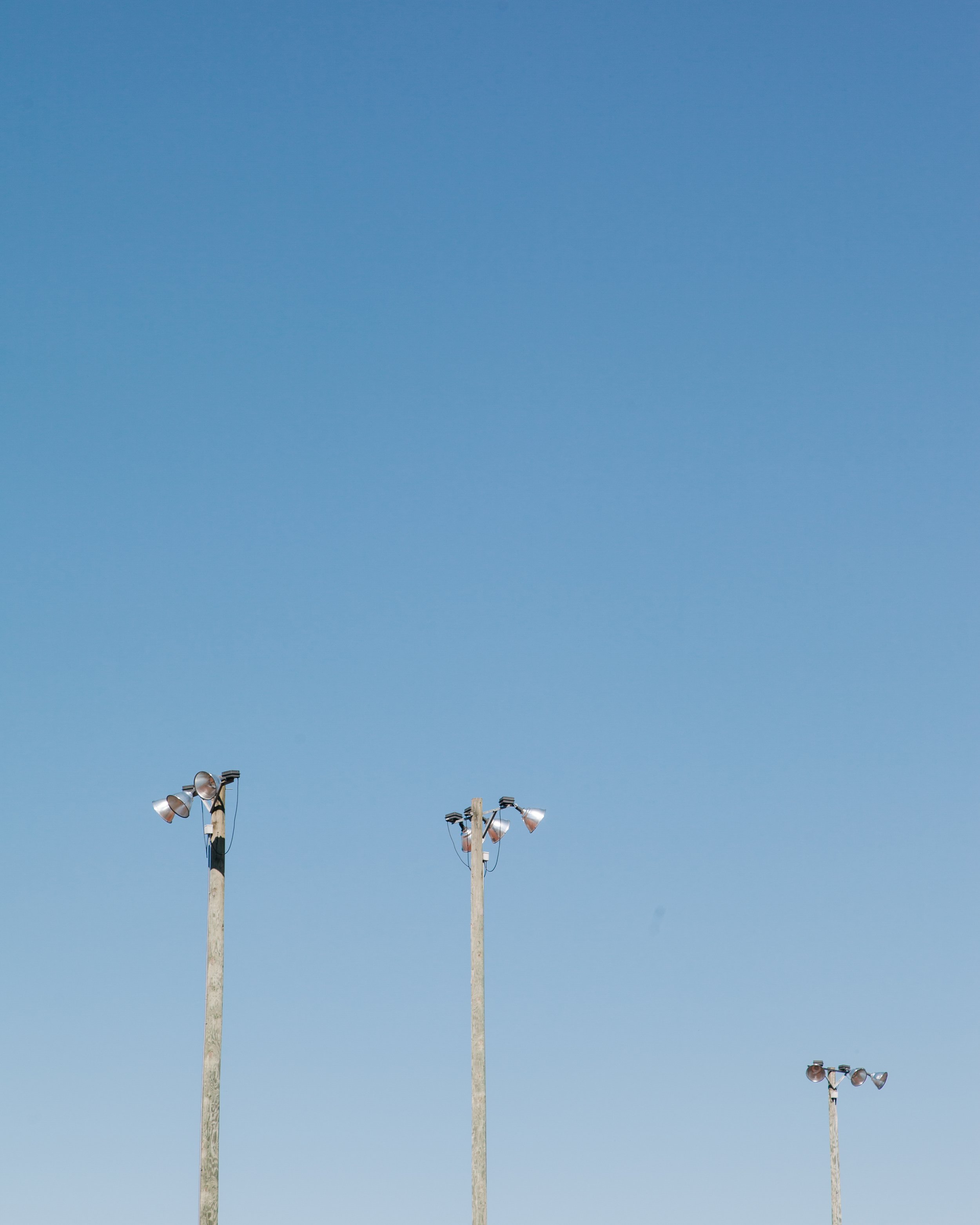 Two tall light poles with multiple floodlights attached, set against a clear blue sky.