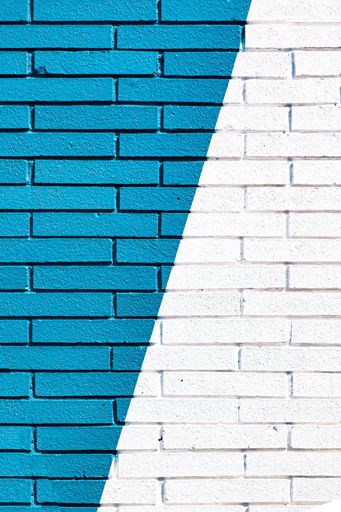 Close-up of a brick wall painted with half blue and half white color, with a diagonal line dividing the two sections.