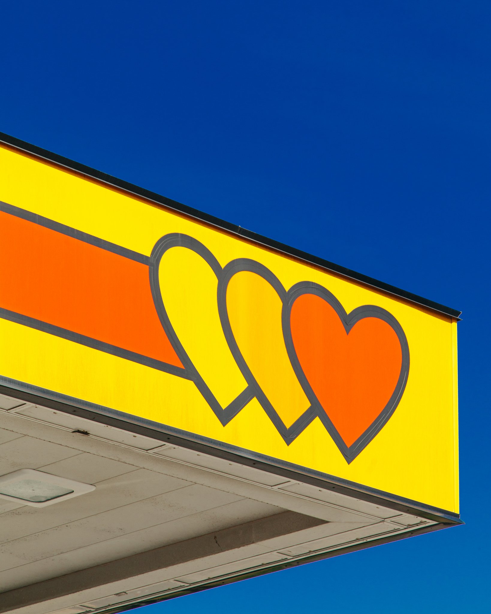 Close-up of a bright yellow and orange retail store sign with a graphic design, set against a clear blue sky.