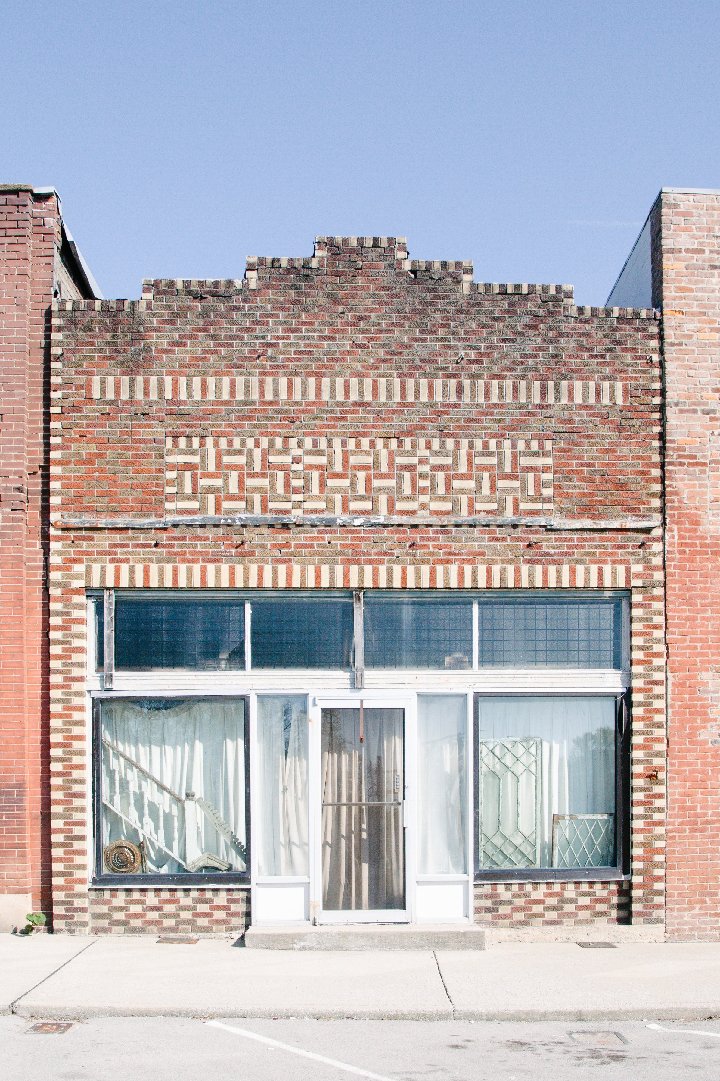 Facade of a brick building with large glass windows and a glass door, under a clear blue sky.