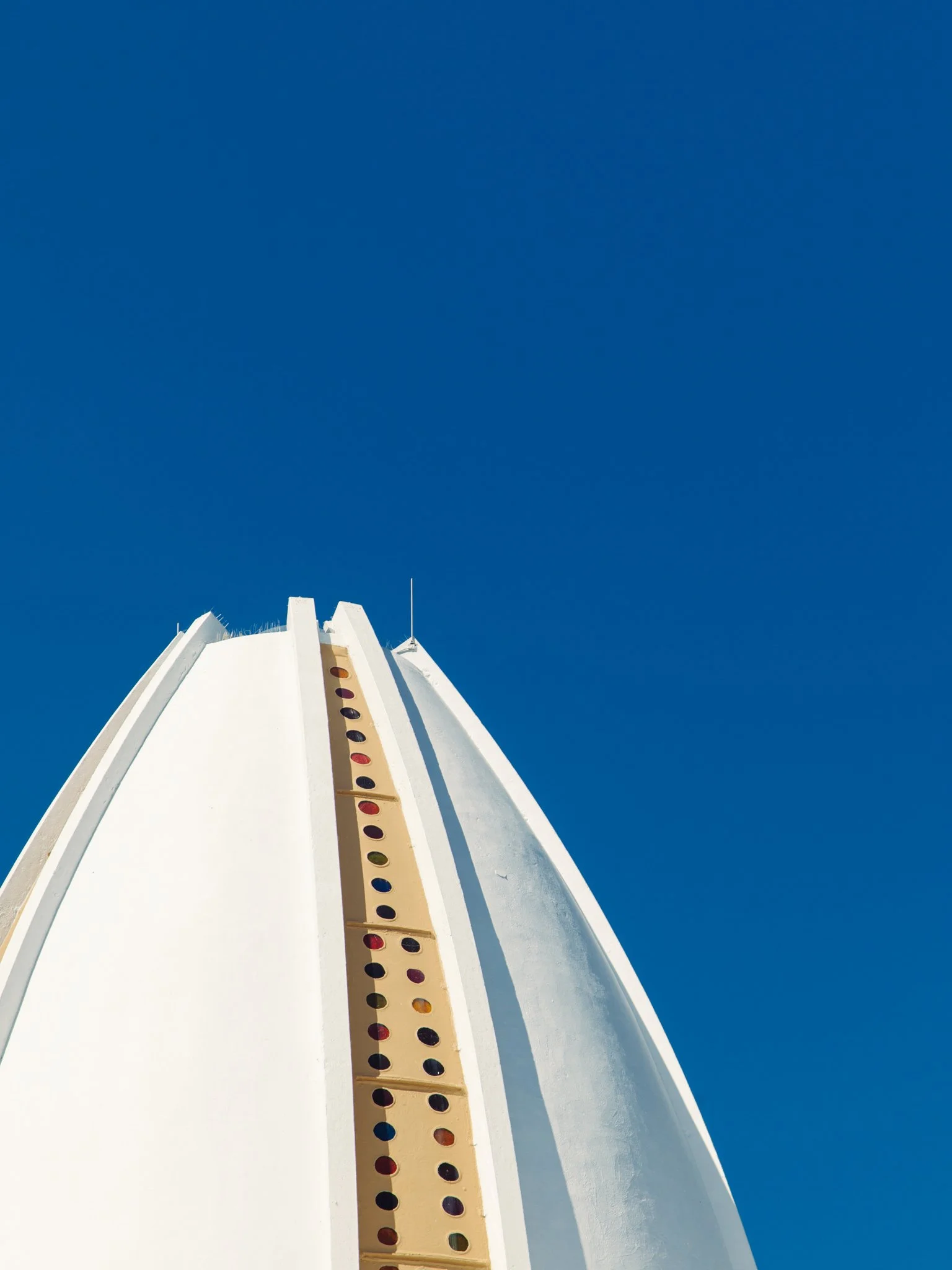 Looking up at a white building with a yellow and red polka-dot pattern, set against a clear blue sky.