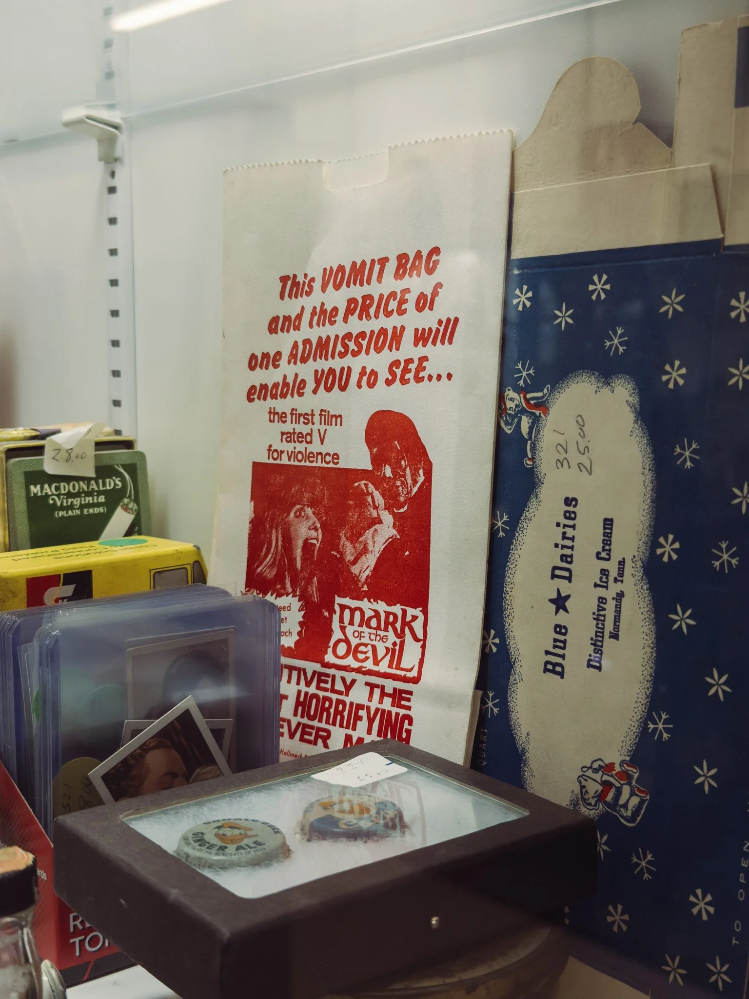 Display of vintage pins in a glass case, supermarket shelf with snack bags, and promotional posters.