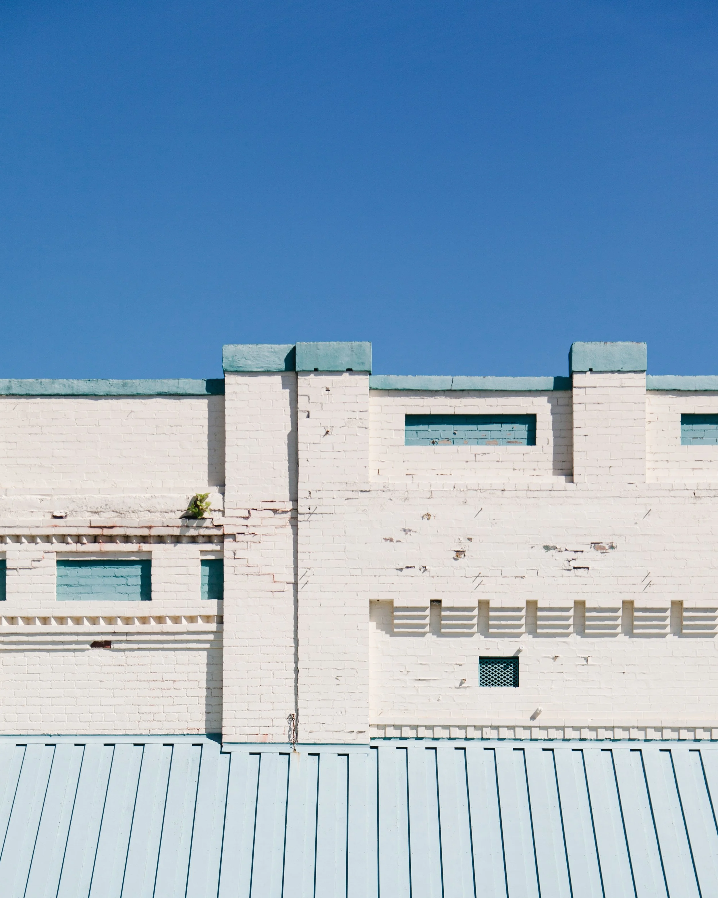 White brick building with small, rectangular windows and a light blue roof, under a clear blue sky.