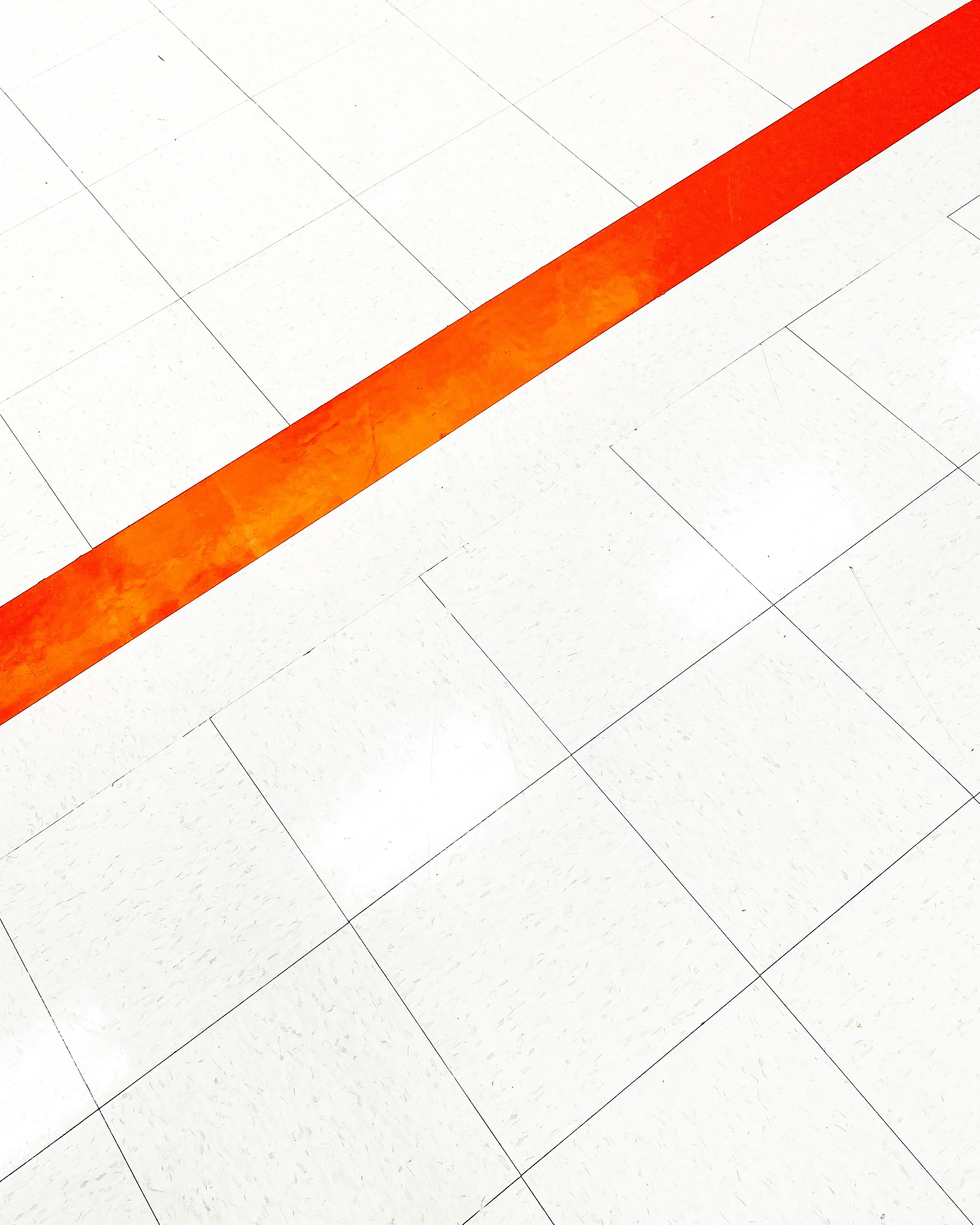 Close-up view of white tiled floor with a single orange line strip.