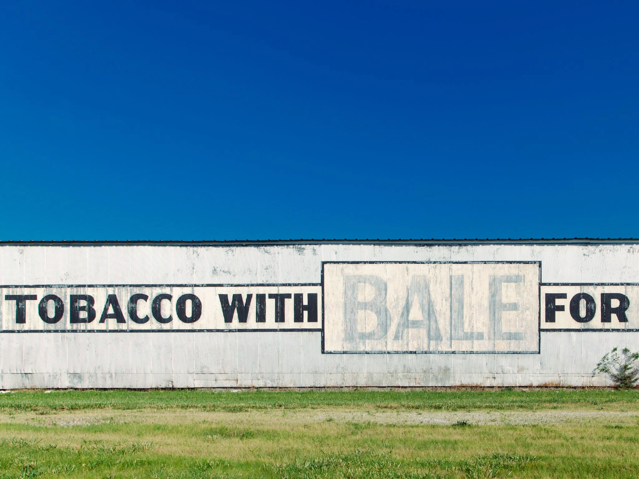 A weathered white building with a sign that reads 'TOBACCO WITH' and a smaller sign partially visible below.
