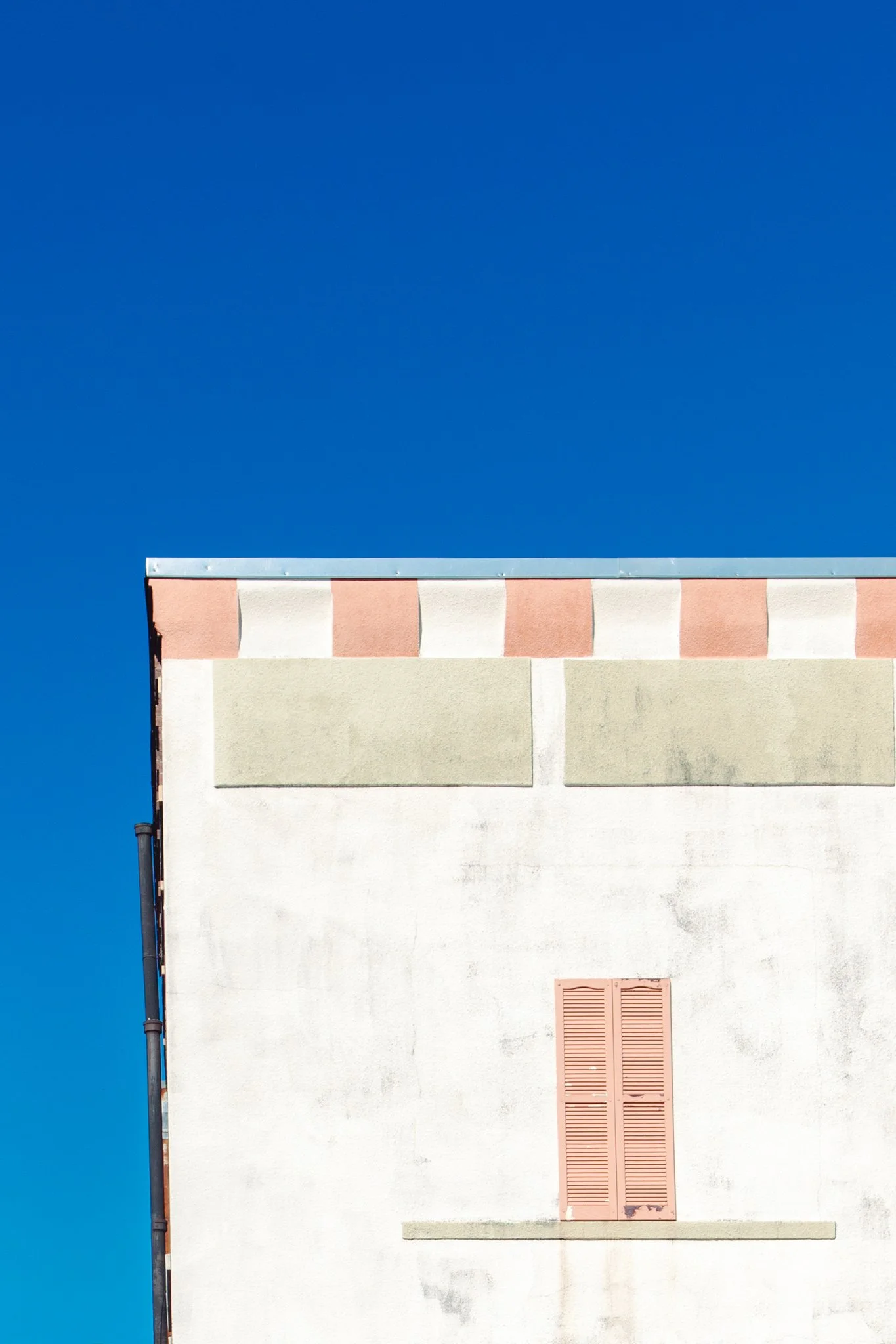 The upper part of a building with a white wall, pink shutters, and a blue sky.