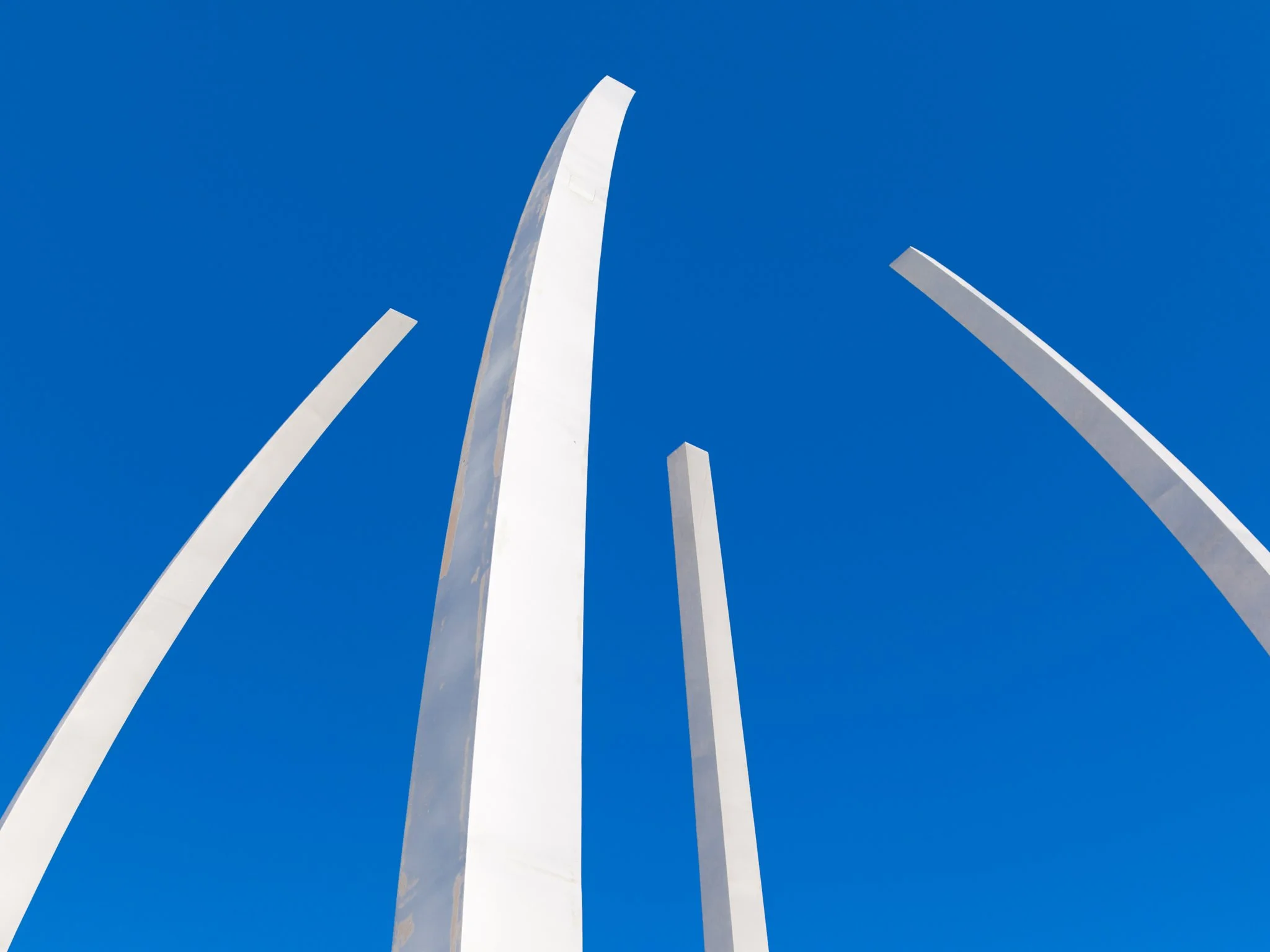 Low-angle view of tall white modern sculptures against a clear blue sky.