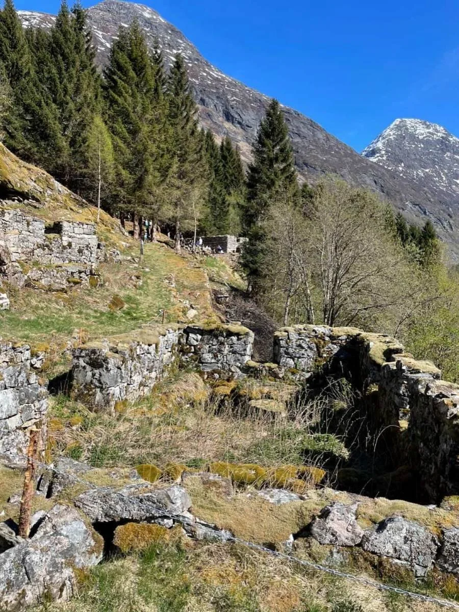 The stone walls of an old cowshed. To the left is a farmhouse (Larsbruket). In the background is a cowshed. (Nilsbruket)