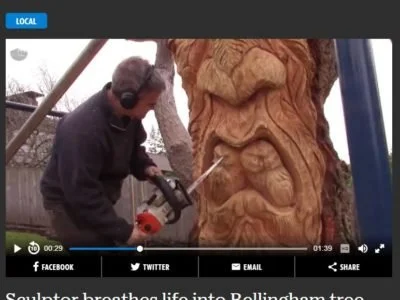 Tomas Vrba using a chainsaw to carve a large wooden tree spirit sculpture into a tree stump in the Seattle area.