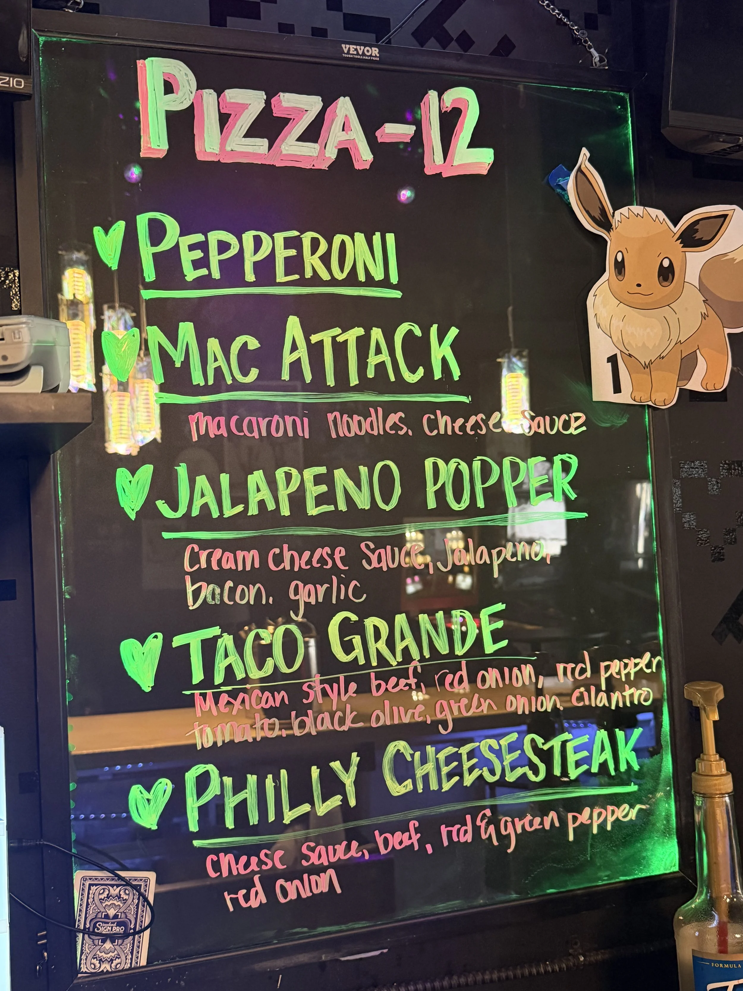 Neon sign menu featuring pizza options such as Pizza-12, Pepperoni, Mac Attack, Jalapeno Popper, Taco Grande, Philly Cheesesteak, and Philly Cheesesteak, with colorful text and a cartoon Eevee from Pokémon on the side.
