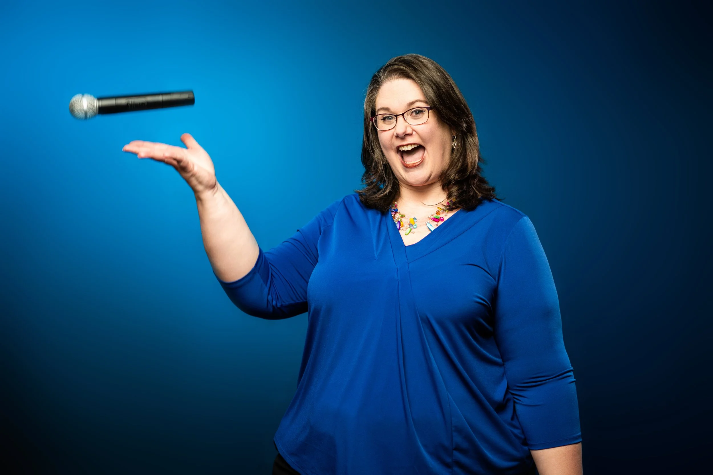 Lauren Ansley, conference emcee and audience engagement specialist, tossing a microphone and smiling on stage.