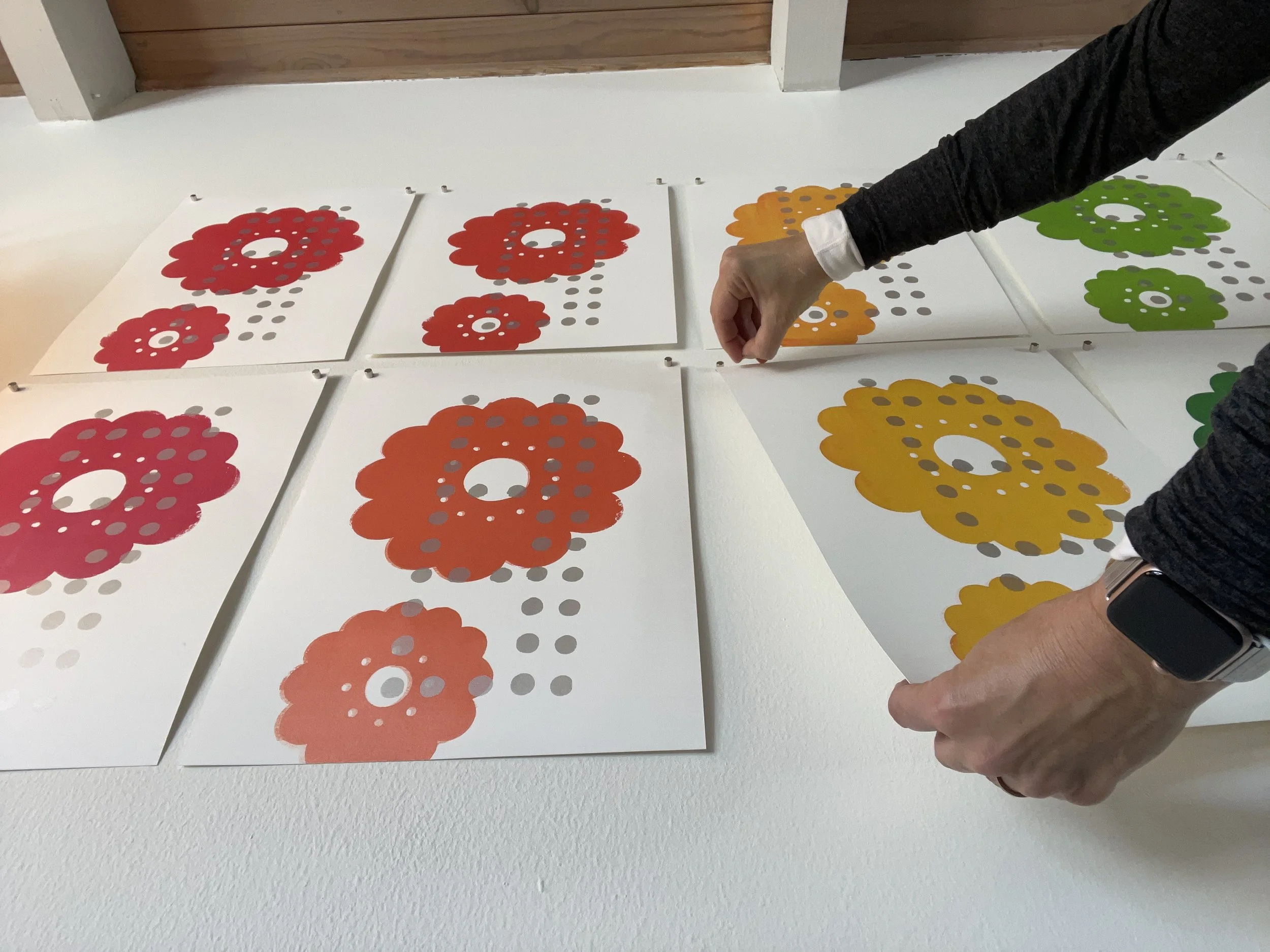 A person arranging colorful flower-shaped cutouts with circular patterns on a white table.