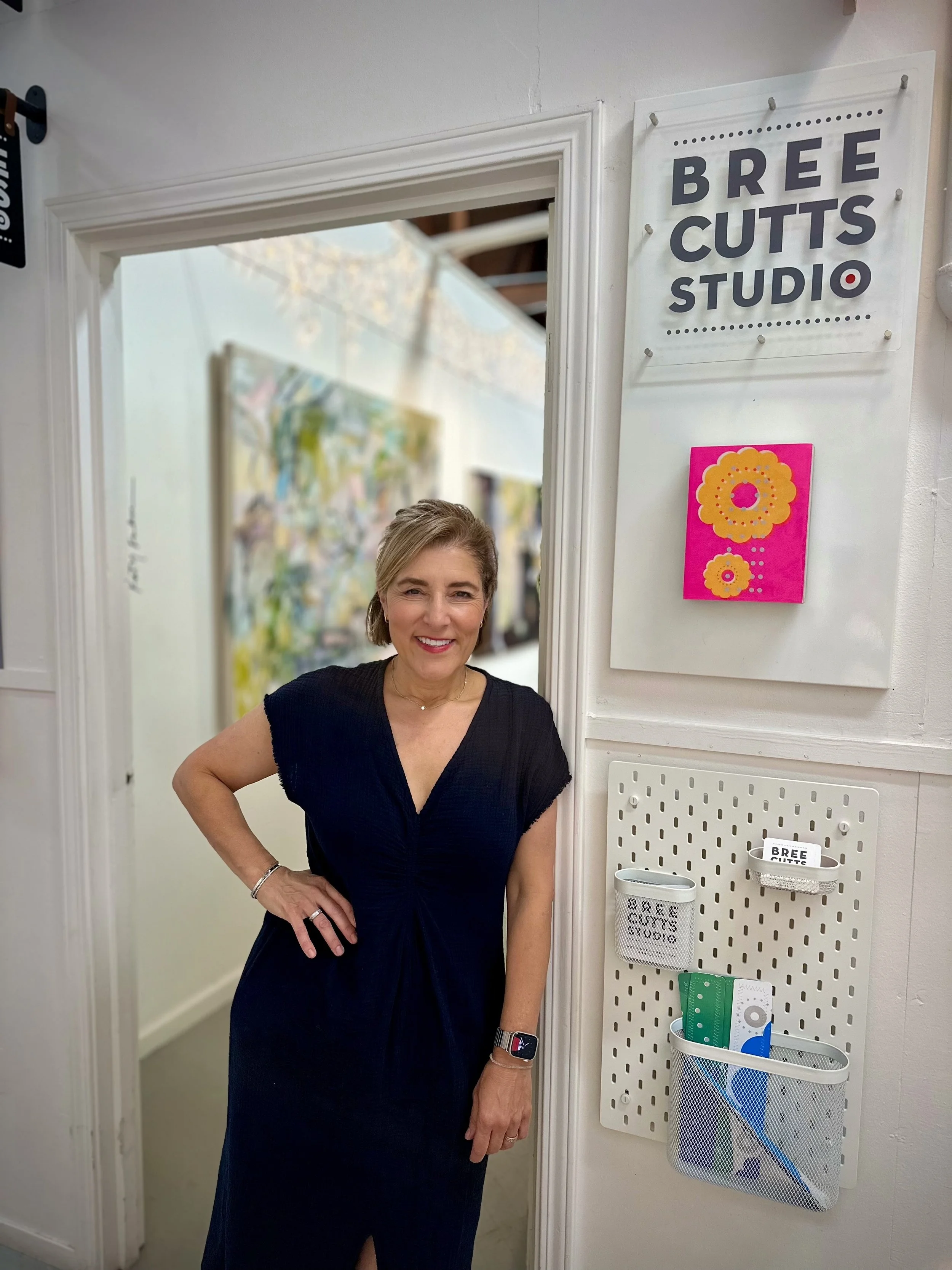 A woman standing inside a studio with a sign that reads 'Bree Cutts Studio' on the wall.