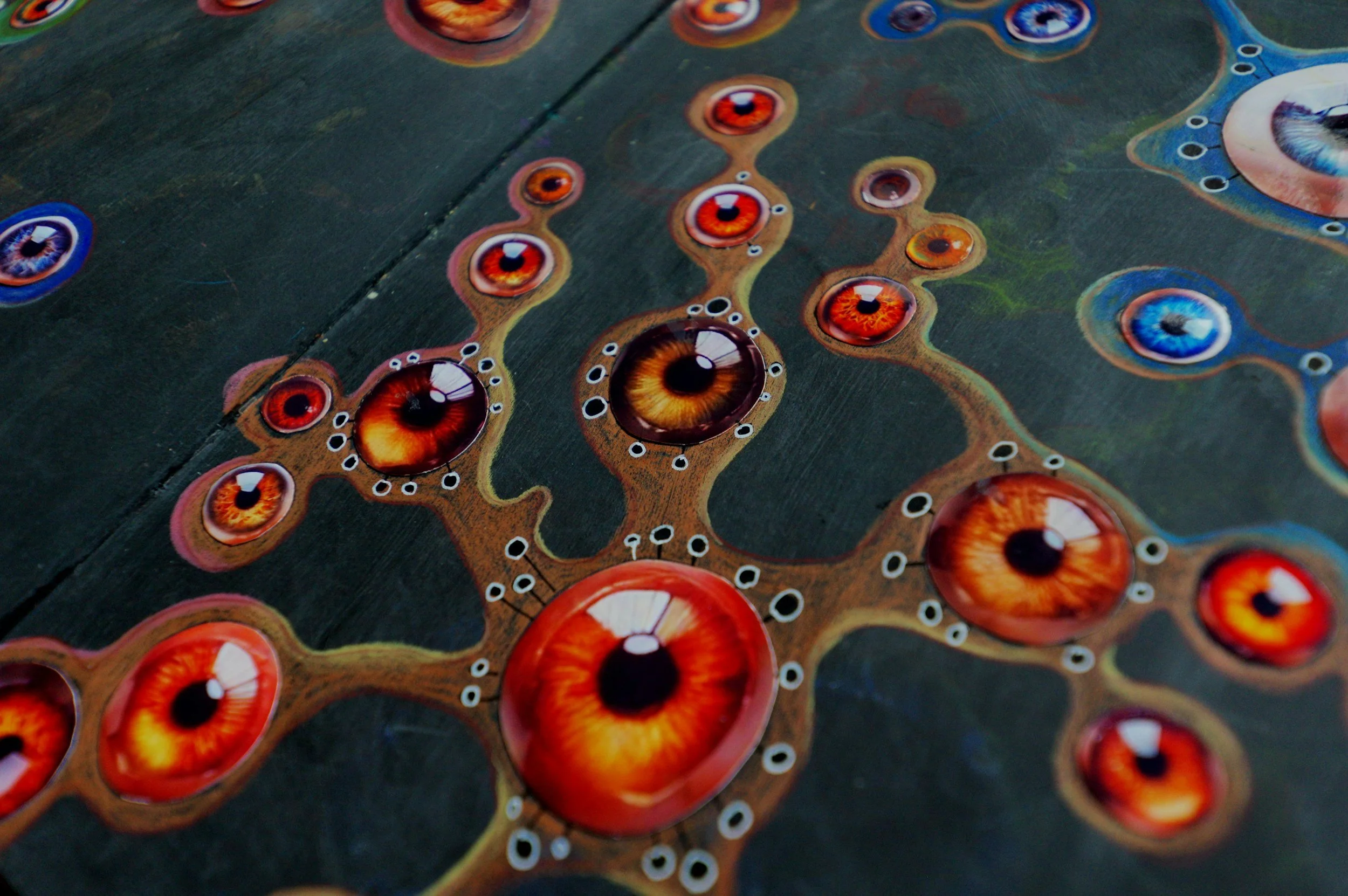 Close-up of a colorful abstract art piece featuring numerous stylized eyeballs with vibrant colors and swirling patterns.