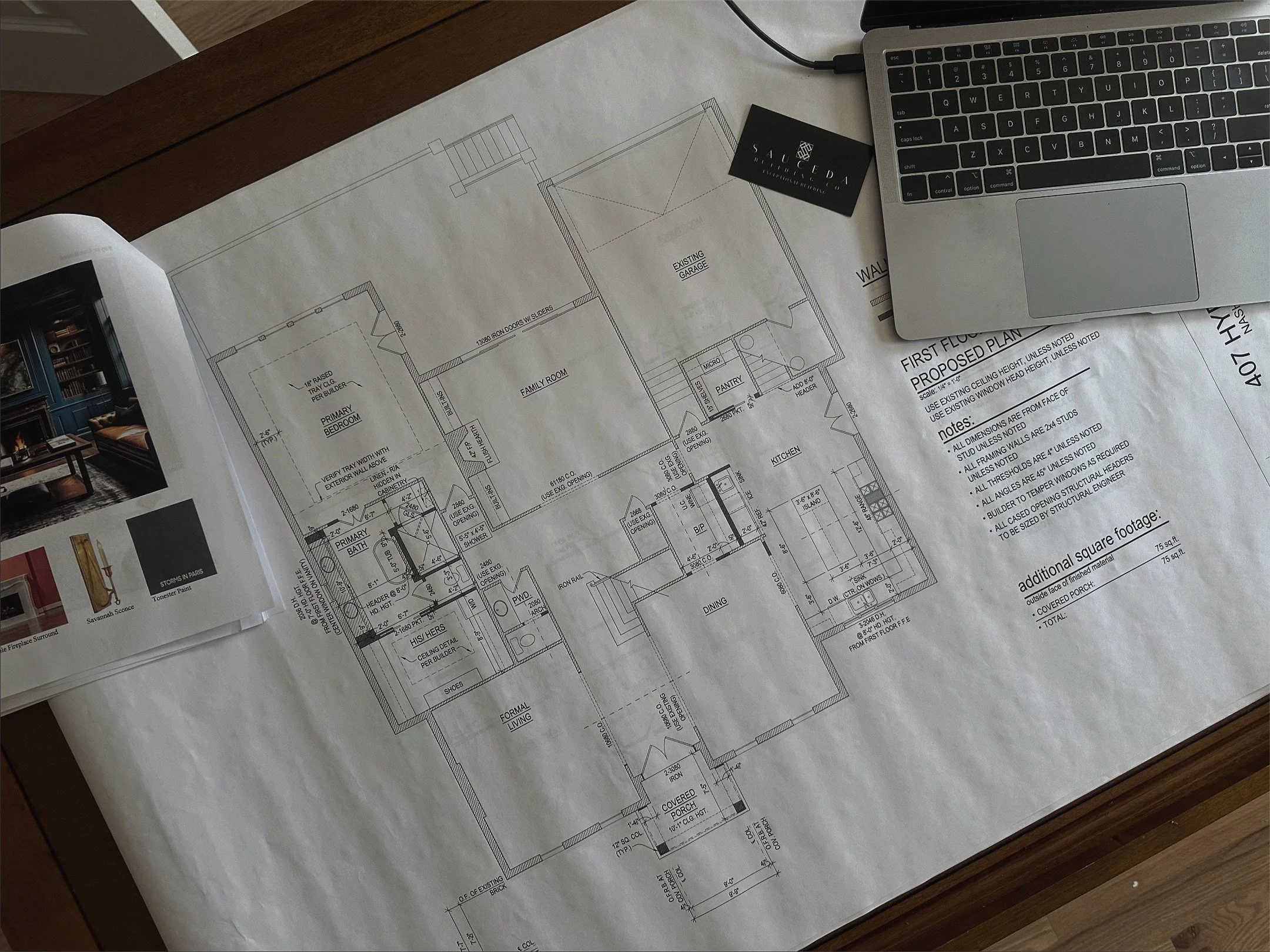 Architectural blueprint of a house layout with a laptop, business card, and magazine on the desk.