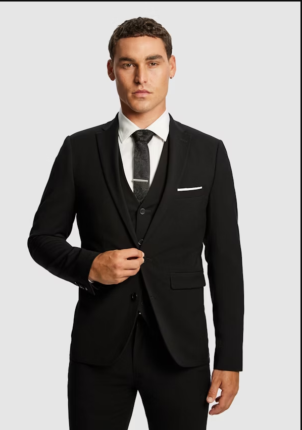 Young man in a black suit with a white shirt and black tie posing against a neutral background.