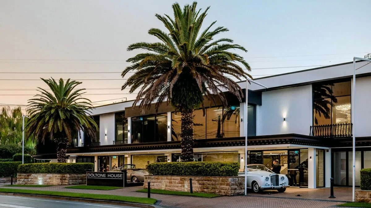 Modern building with palm trees and vintage cars parked outside.