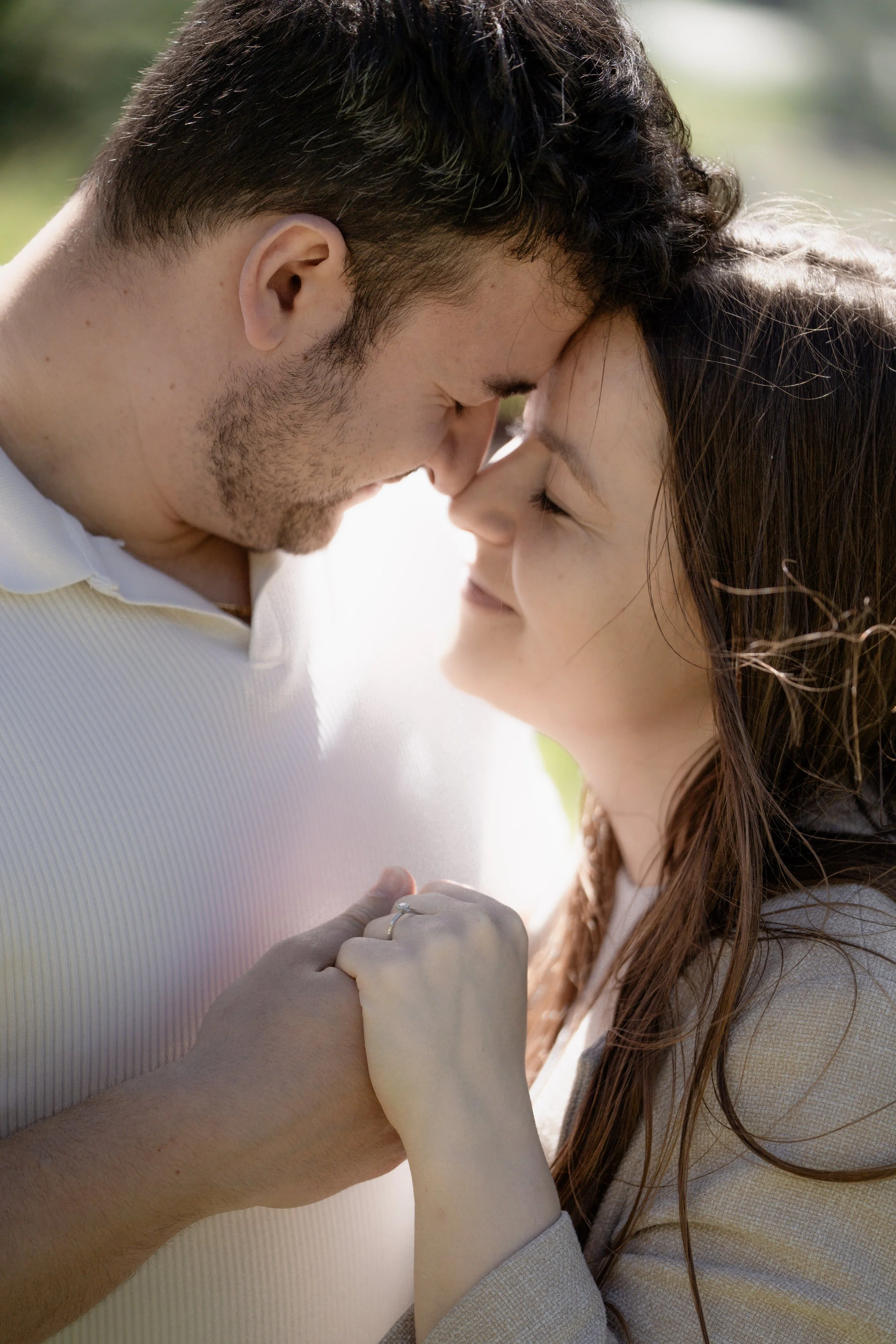 Paar, das mit geschlossenen Augen bei Sonnenlicht zusammengedrückt und lächelnd miteinander innig schmust.