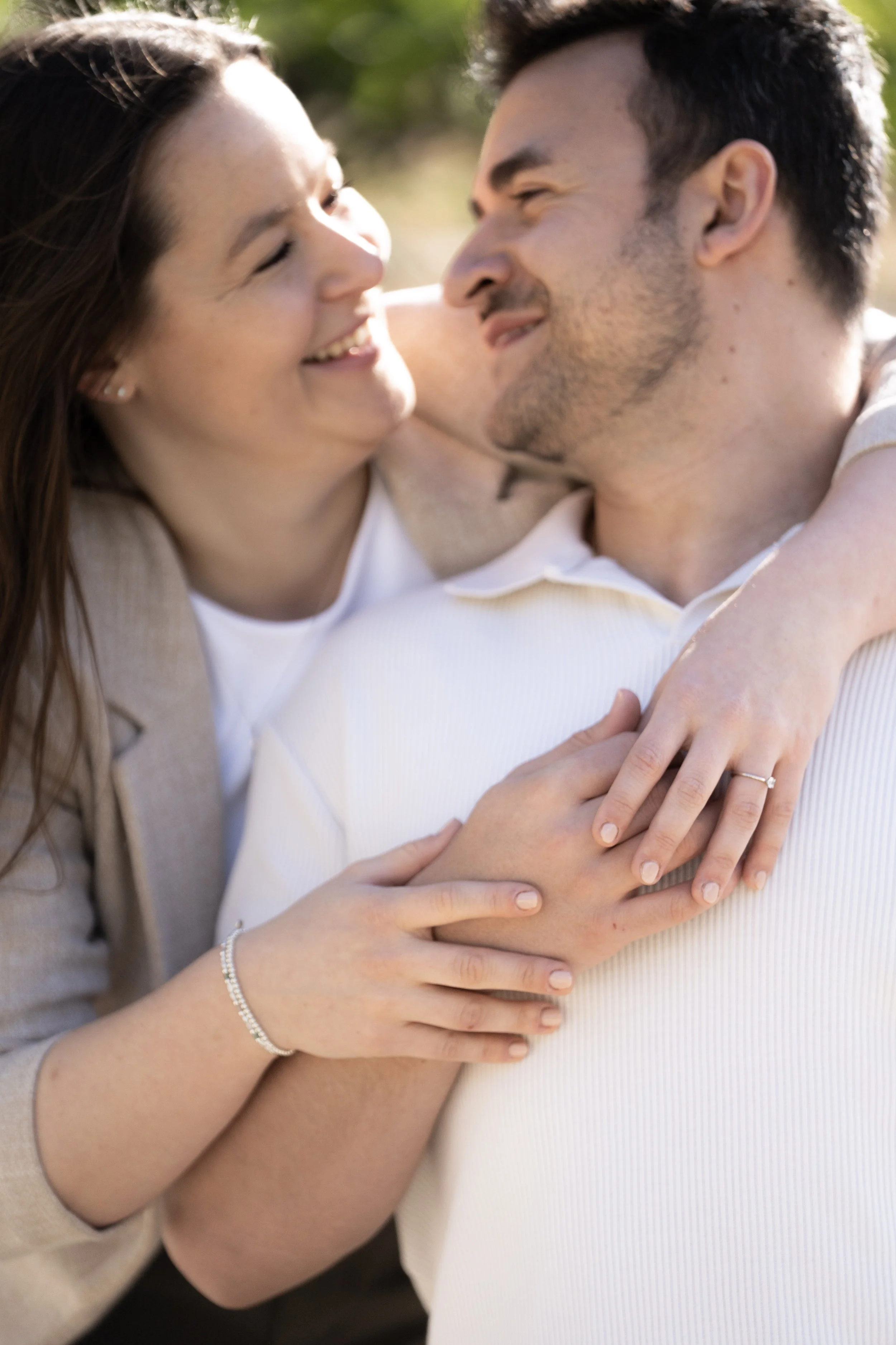 Ein lachendes Paar umarmt sich draußen in Sonnenlicht, die Frau trägt einen Ehering.