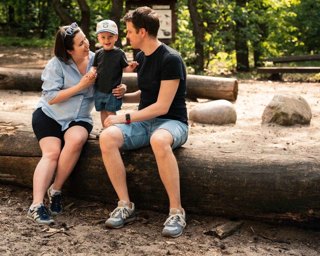 Outdoor family portrait of parents with their young child sitting on a wooden log in a park