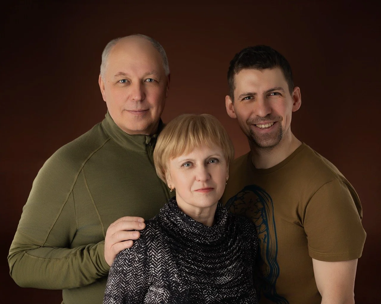 Studio family portrait of three adults on a warm brown background