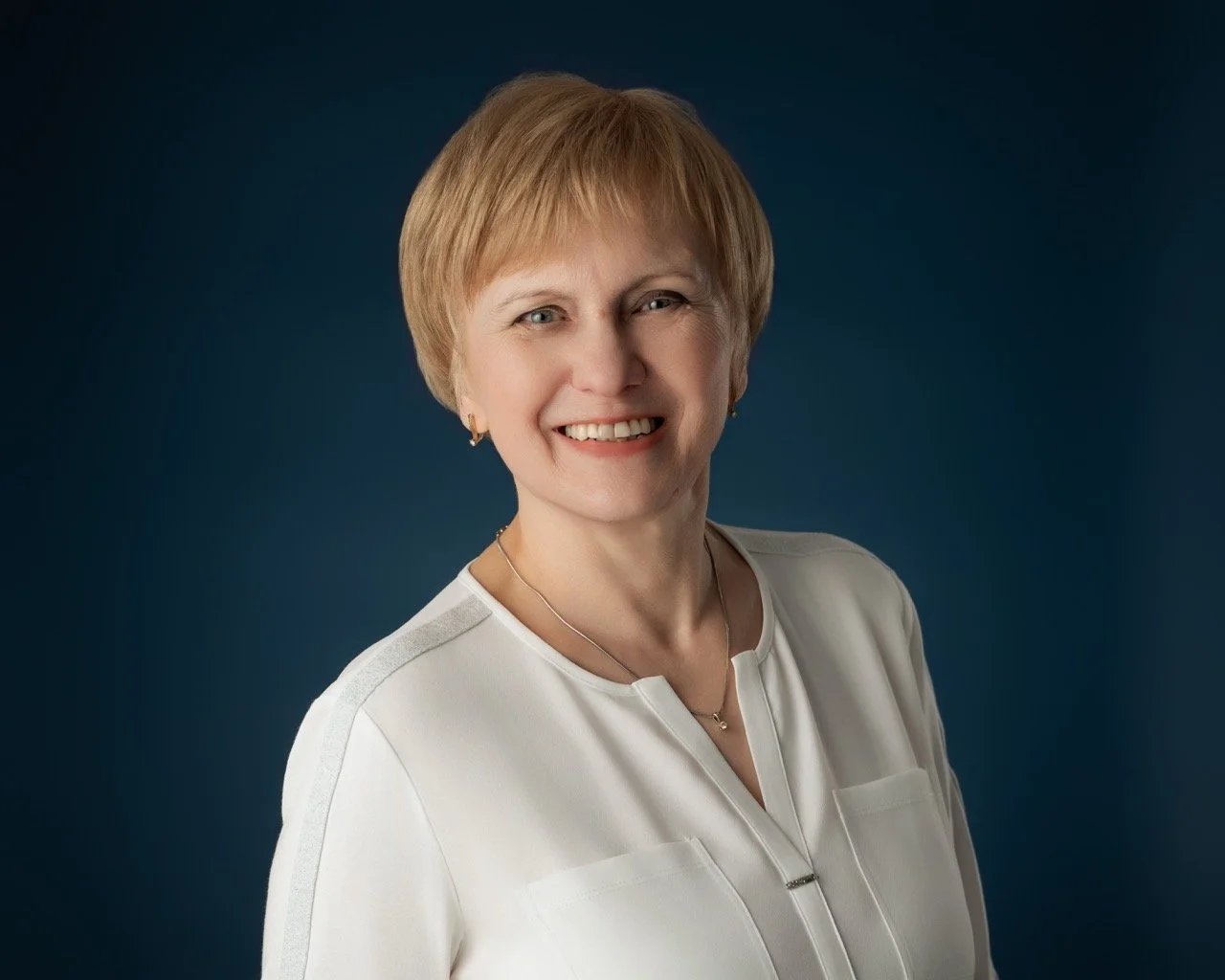 Professional headshot of a smiling woman in a white blouse on a blue background