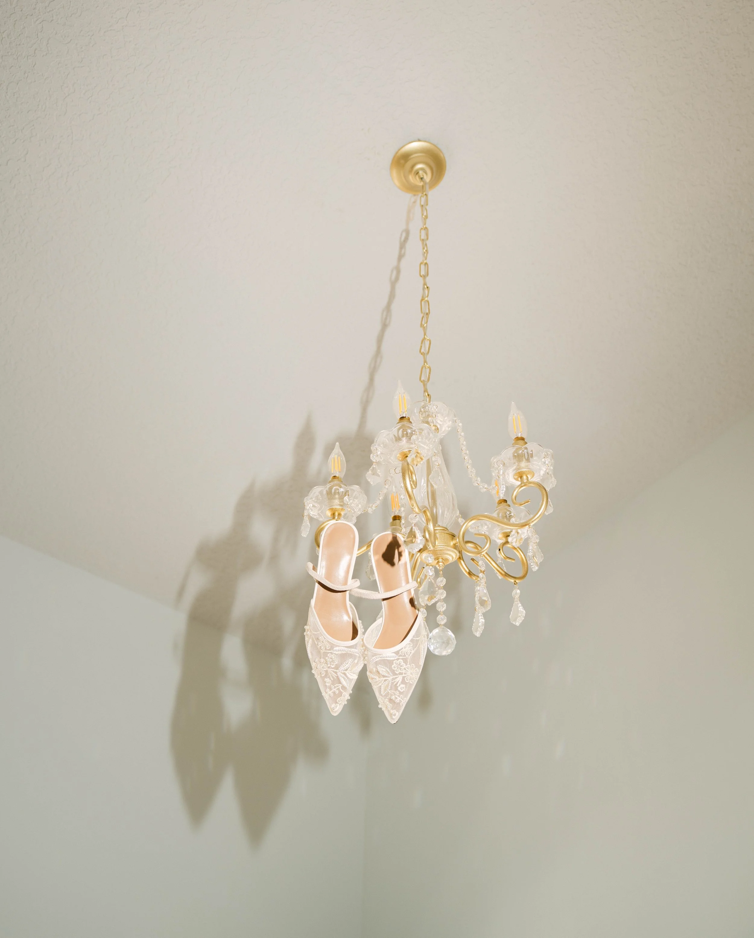 Chandelier hanging from a ceiling with ballet slippers hanging from it.
