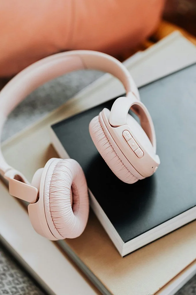 A pair of pink headphones placed on a pile of books on a desk, suggesting a blend of study and leisure.