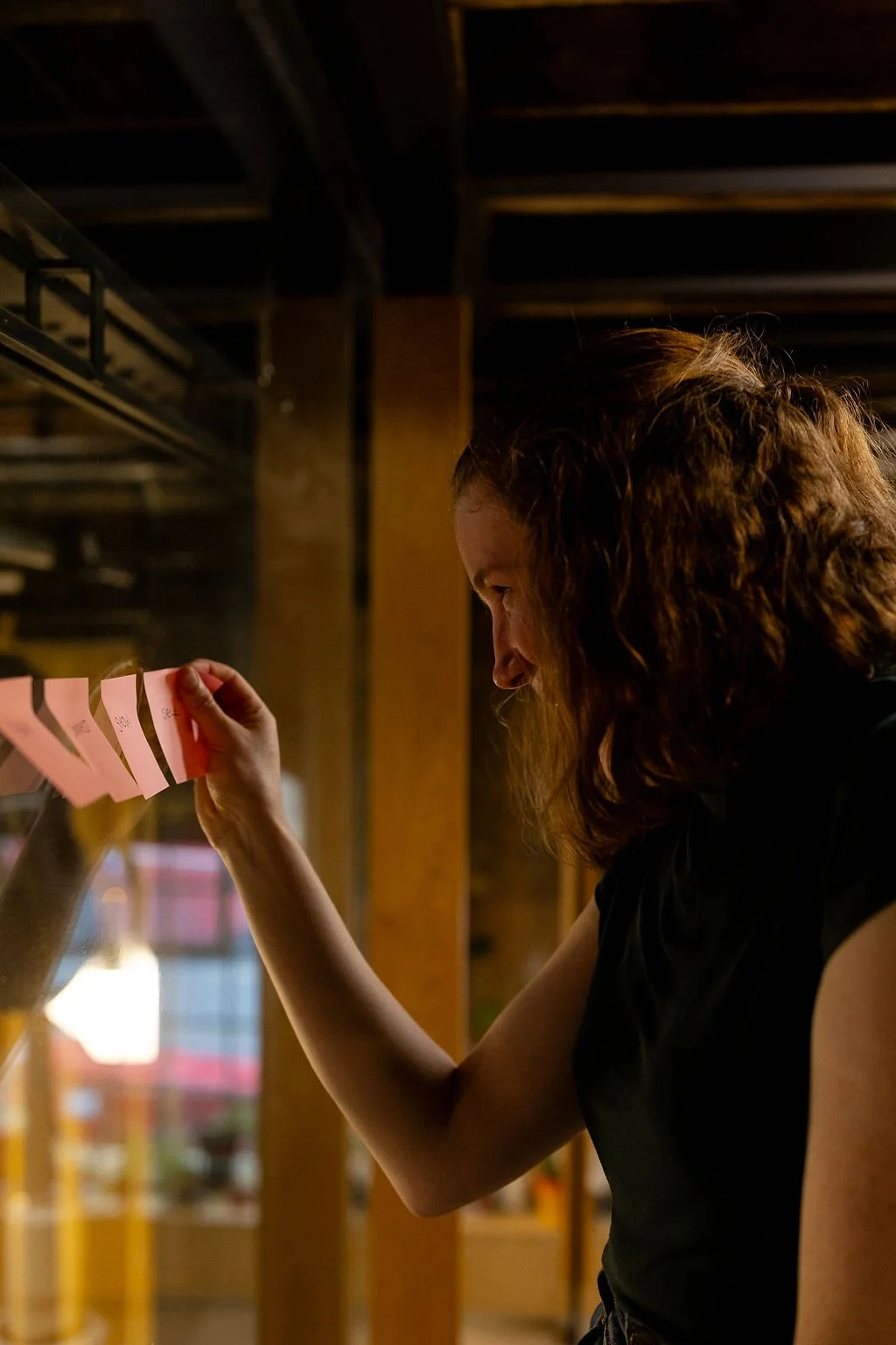 Portrait of brand photographer Beth Hicks stood next to the glass window, placing pink sticky notes on the glass.