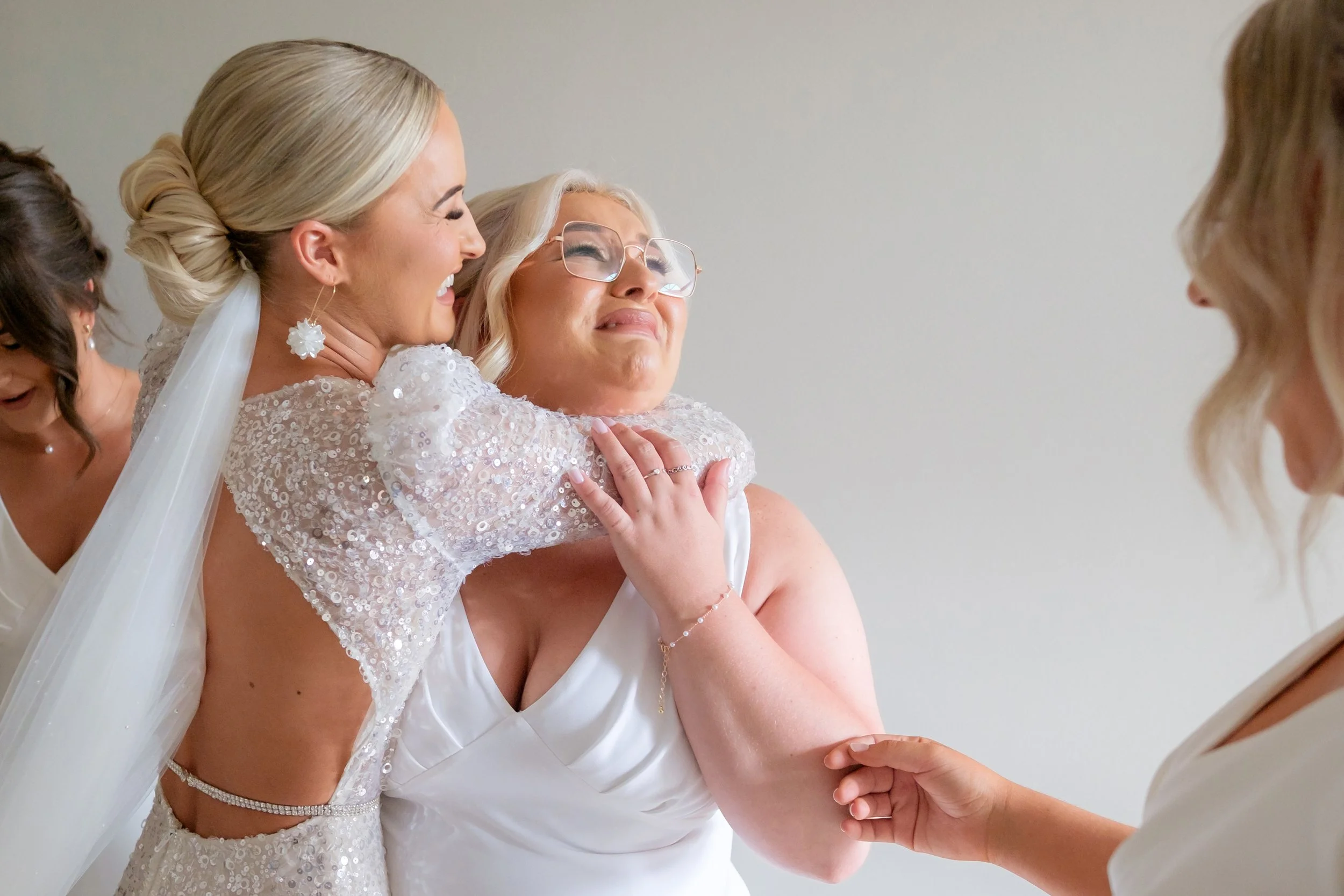 A bride and her bridesmaid sharing an emotional moment, with the bride's arms around her friend.