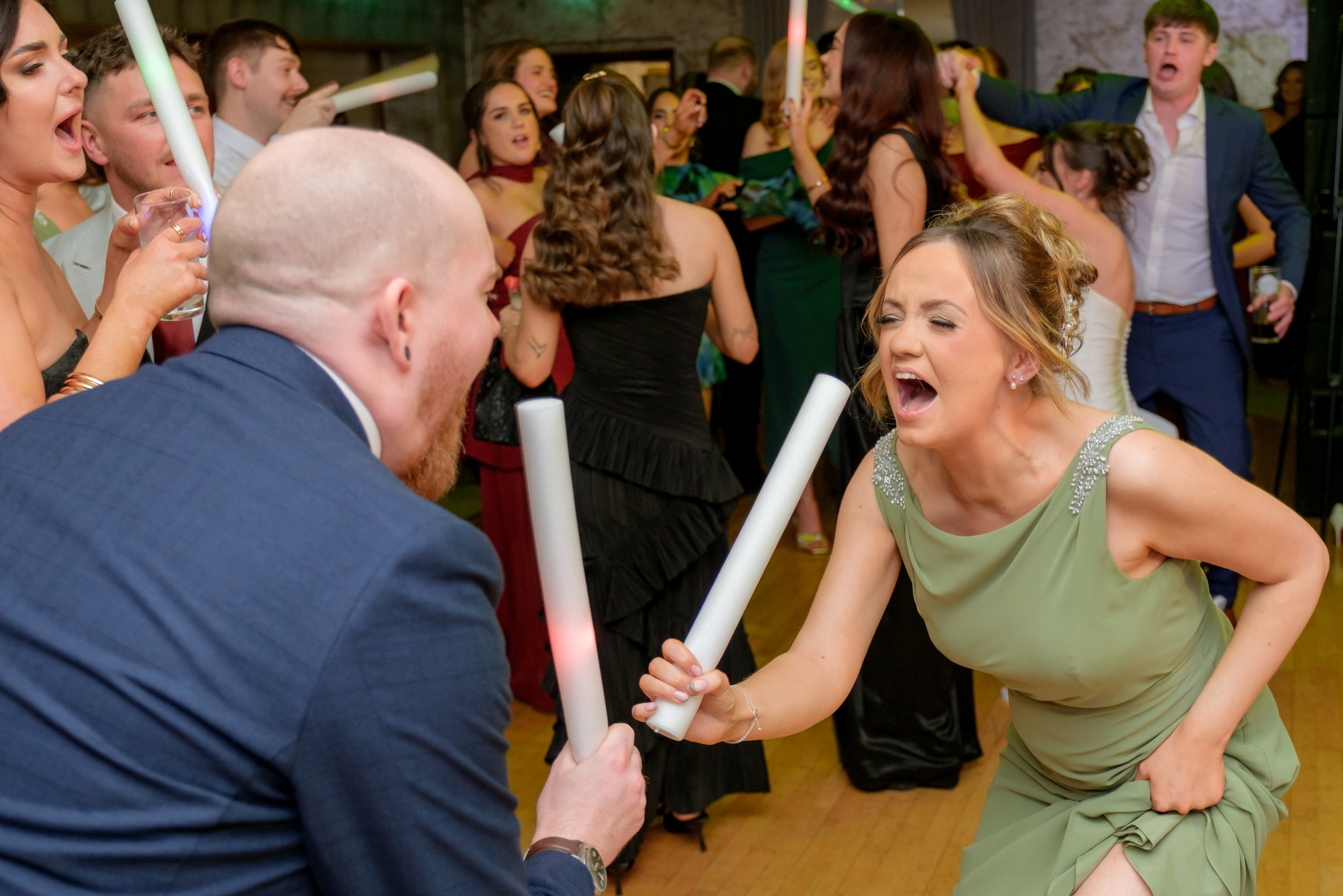 People dancing at a party with some holding glow sticks, expressing excitement or enjoyment.