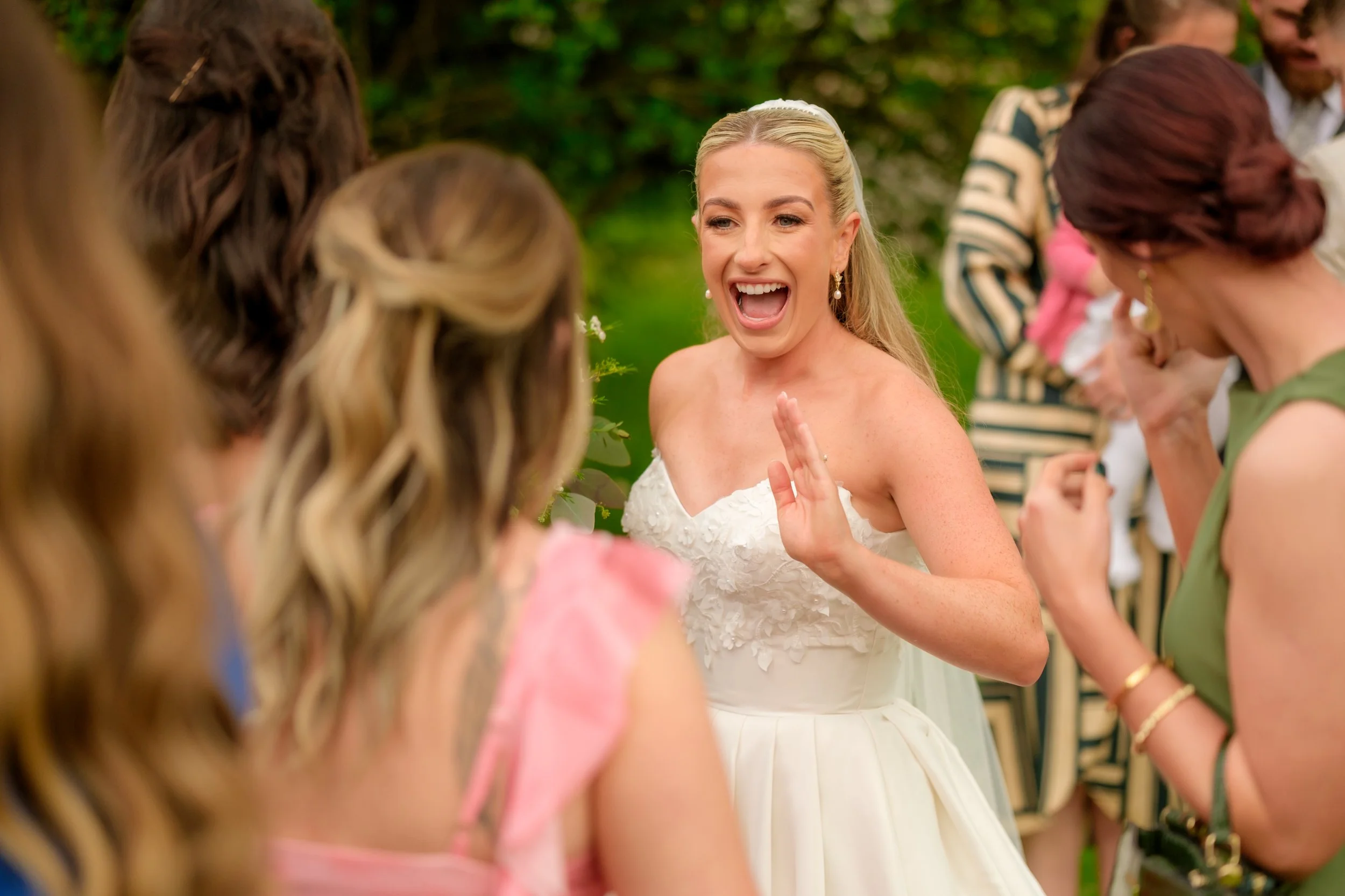 A woman in a wedding dress happily talking to a group of women at an outdoor wedding reception.