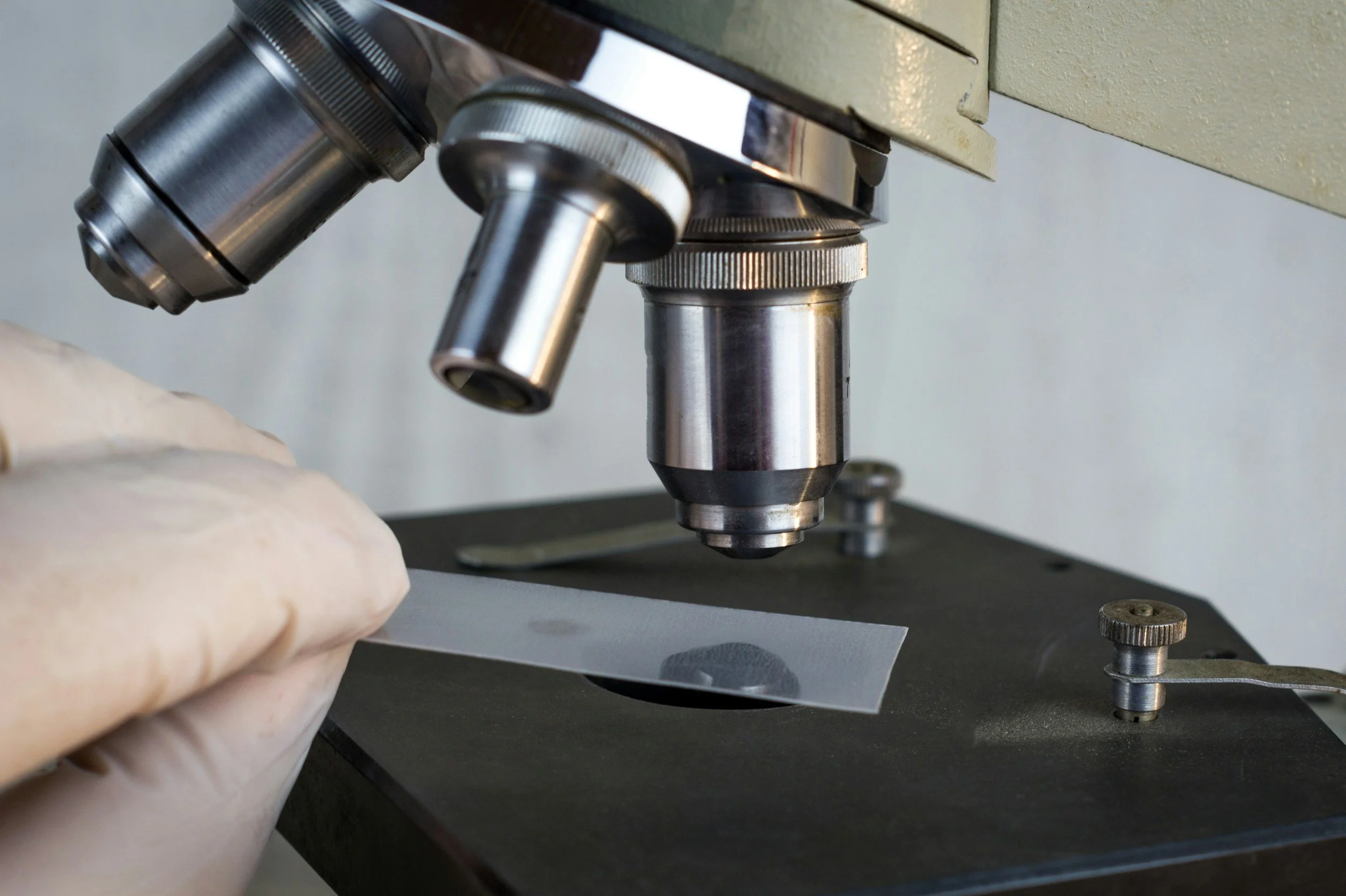 Close-up of a microscope with a hand placing a glass slide under the objective lens.