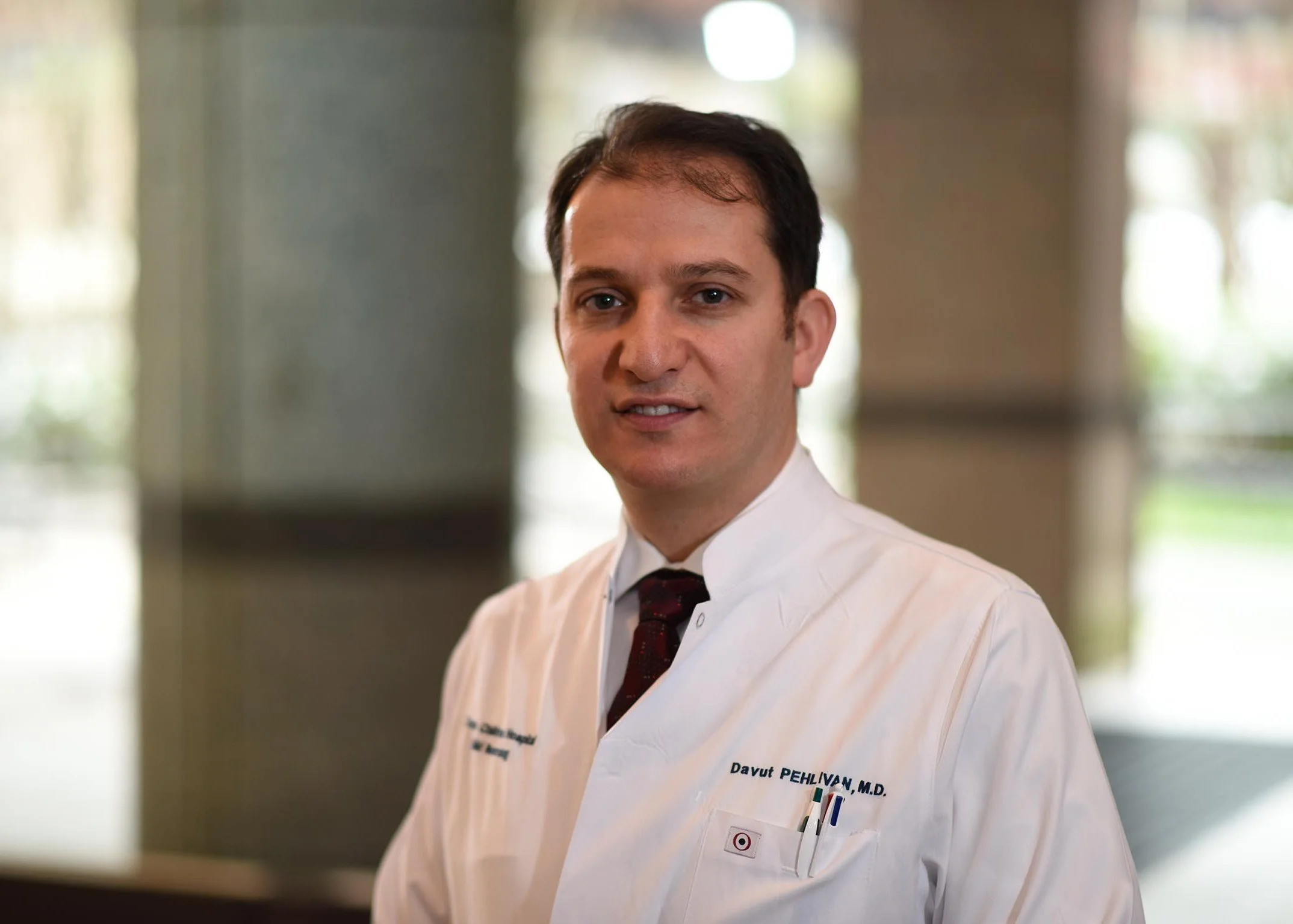 A man in a white medical coat standing indoors.