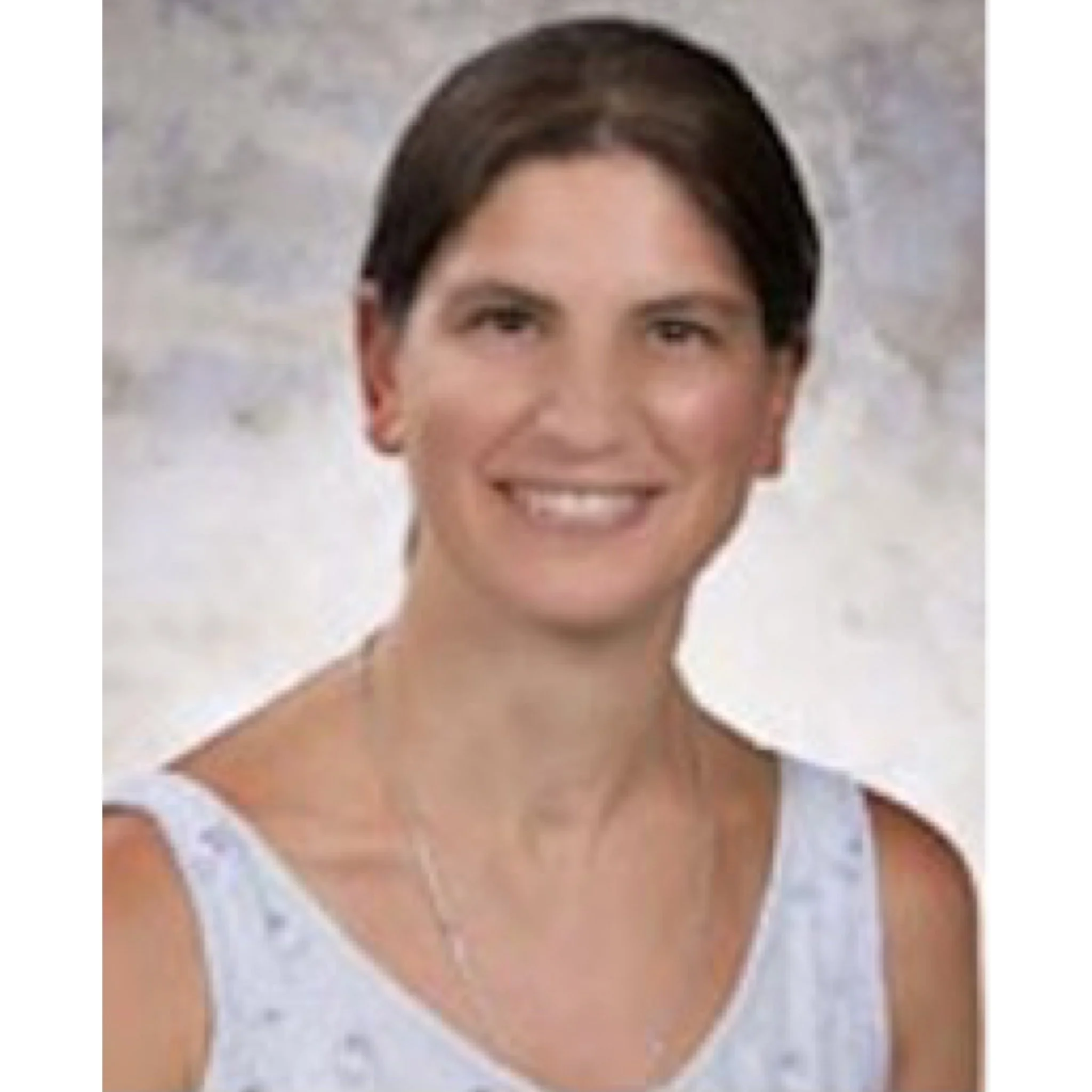 Portrait of a woman with dark hair in a bun, wearing a light-colored sleeveless top, smiling against a neutral background.
