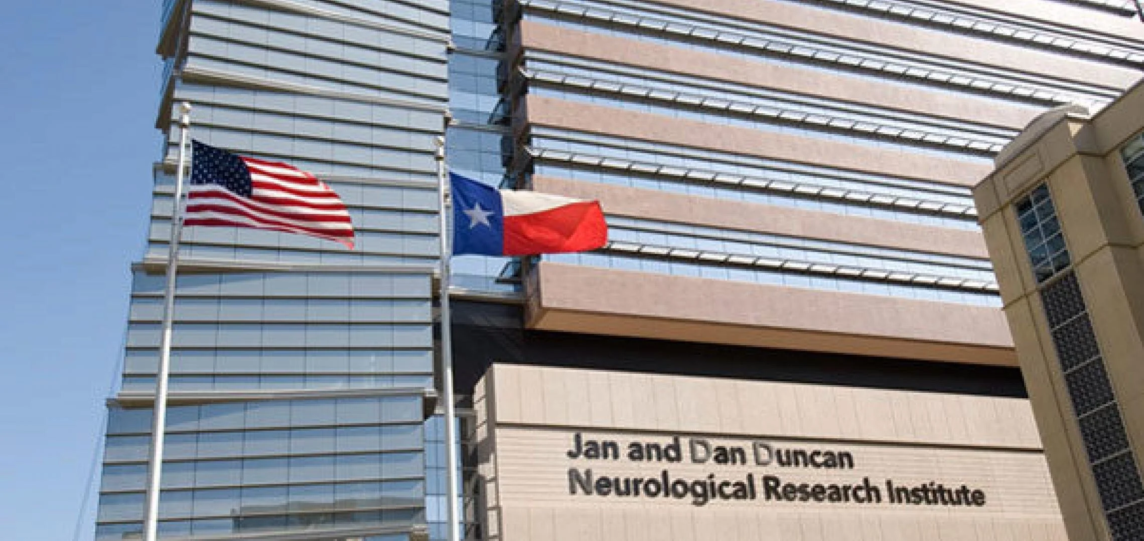 Exterior view of the Jan and Dan Duncan Neurological Research Institute building with American and Texas flags in front.