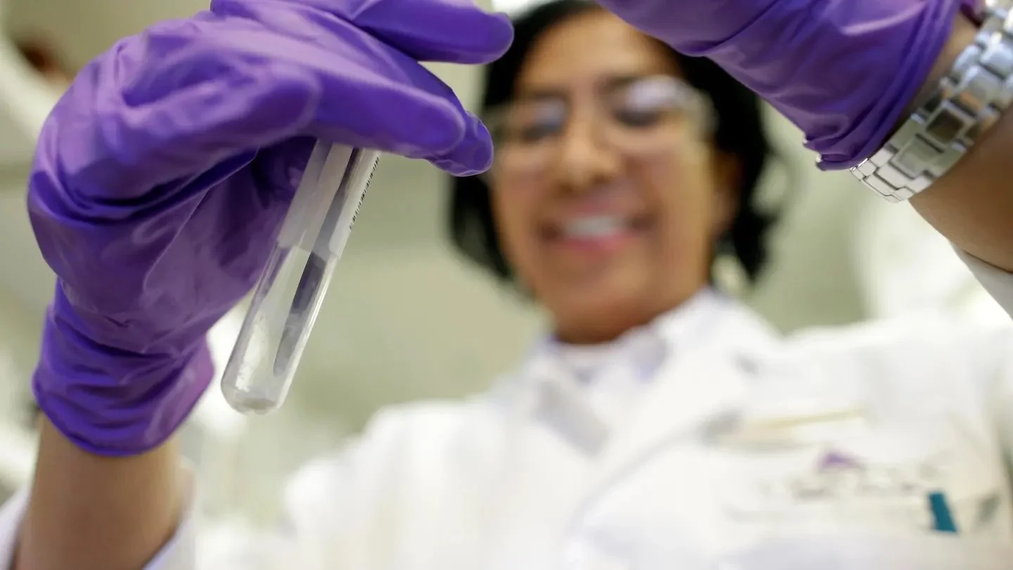 Scientist wearing purple gloves holding a test tube.