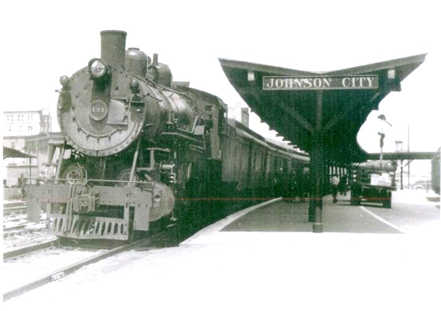 Black and white photo of an old steam train at Johnson City station, with a historical wooden platform canopy.