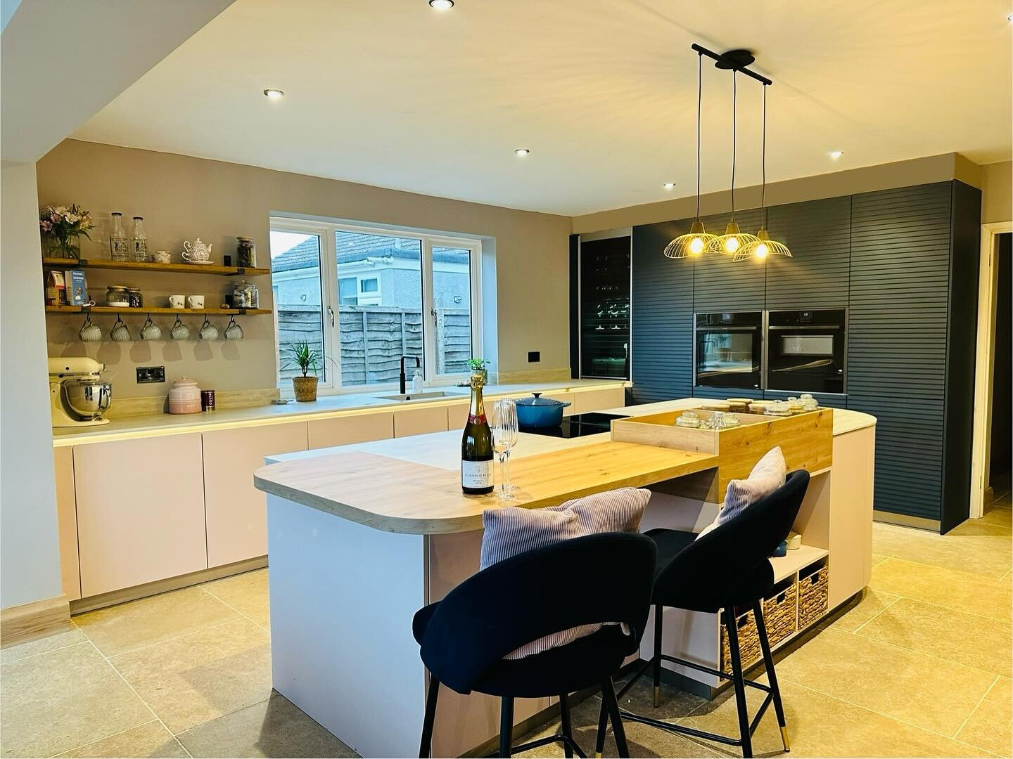 We love it when a plan comes together! The rose pink doors are beautiful framed by the dark blue Scala ribbed tall units by @schueller.kuechen - Limestone worktops which match the Limestone floor by @capietra creates a rimless feel to the modern hand